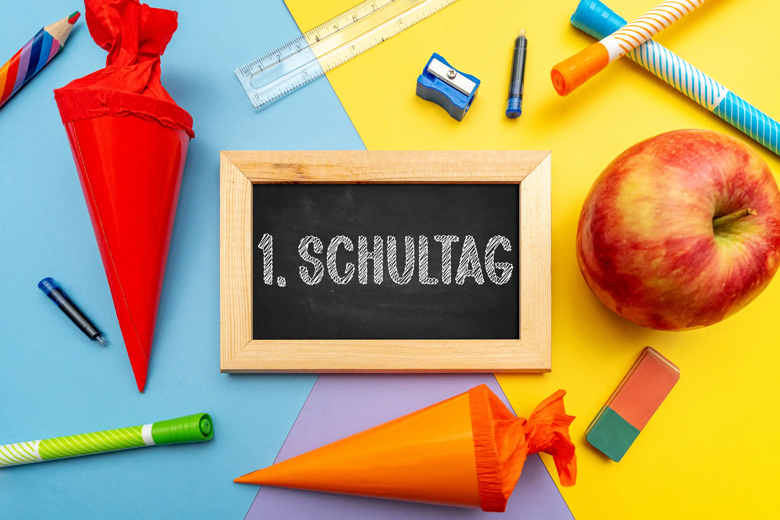 1. Schultag Bild mit schwarzer Schultafel, zwei bunten Schultüten, Apfel und Schulmaterial zum Schulanfang