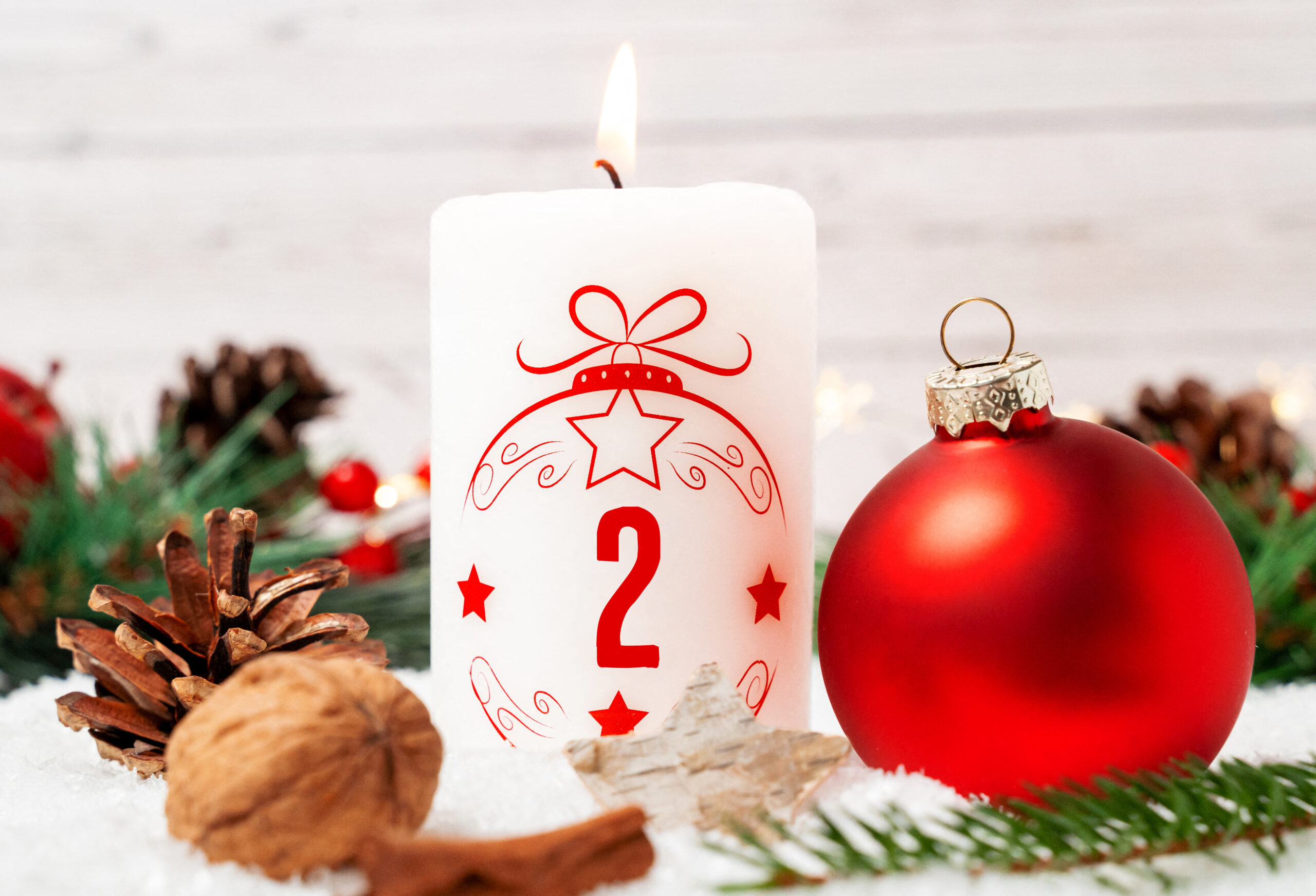 weiße kerze mit roter adventszahl 2 neben roter weihnachtskugel und tannenzweigen zum 2. advent.