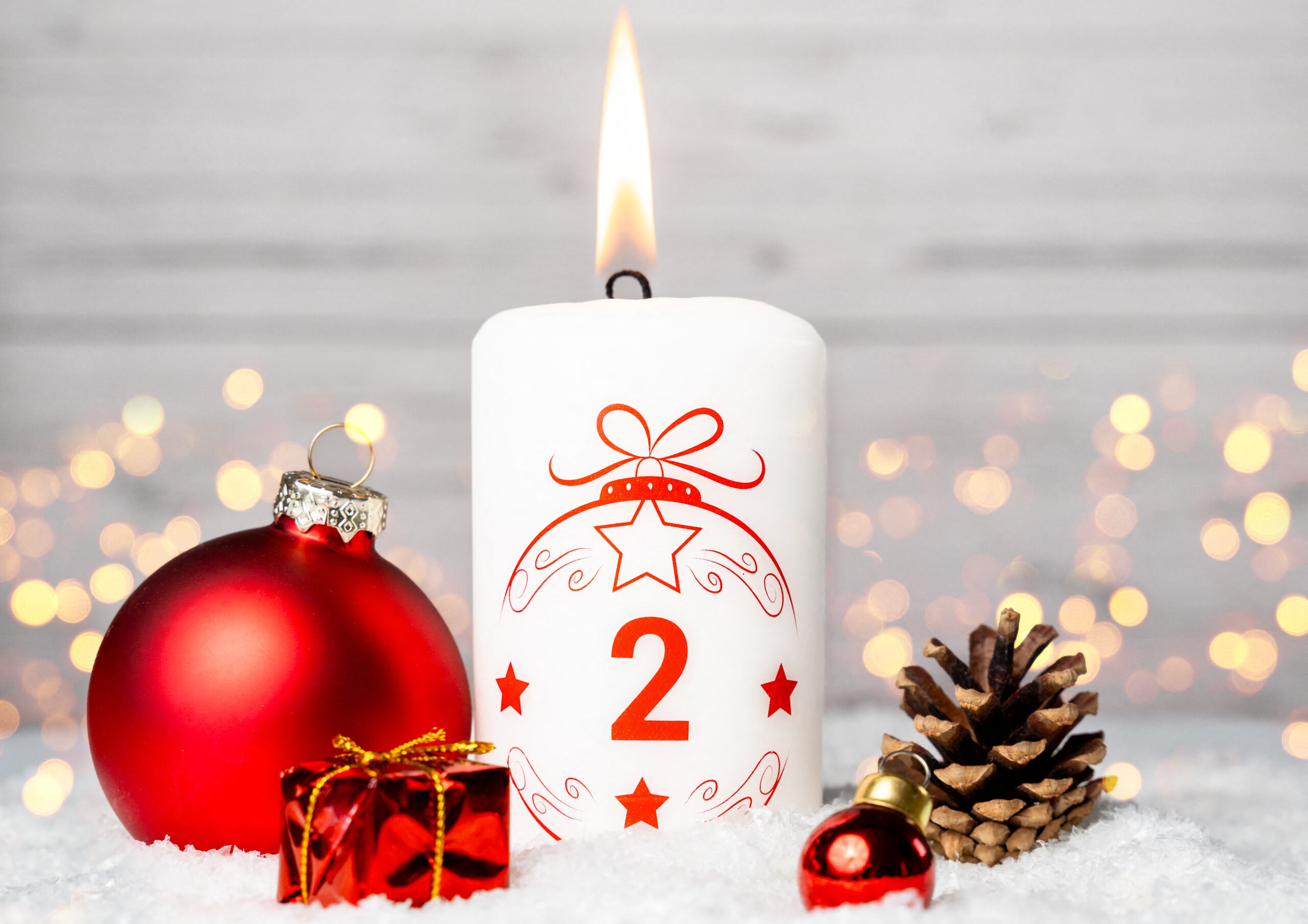 weiße kerze zum 2. adventsabend mit roter weihnachtskugel und deko im schnee