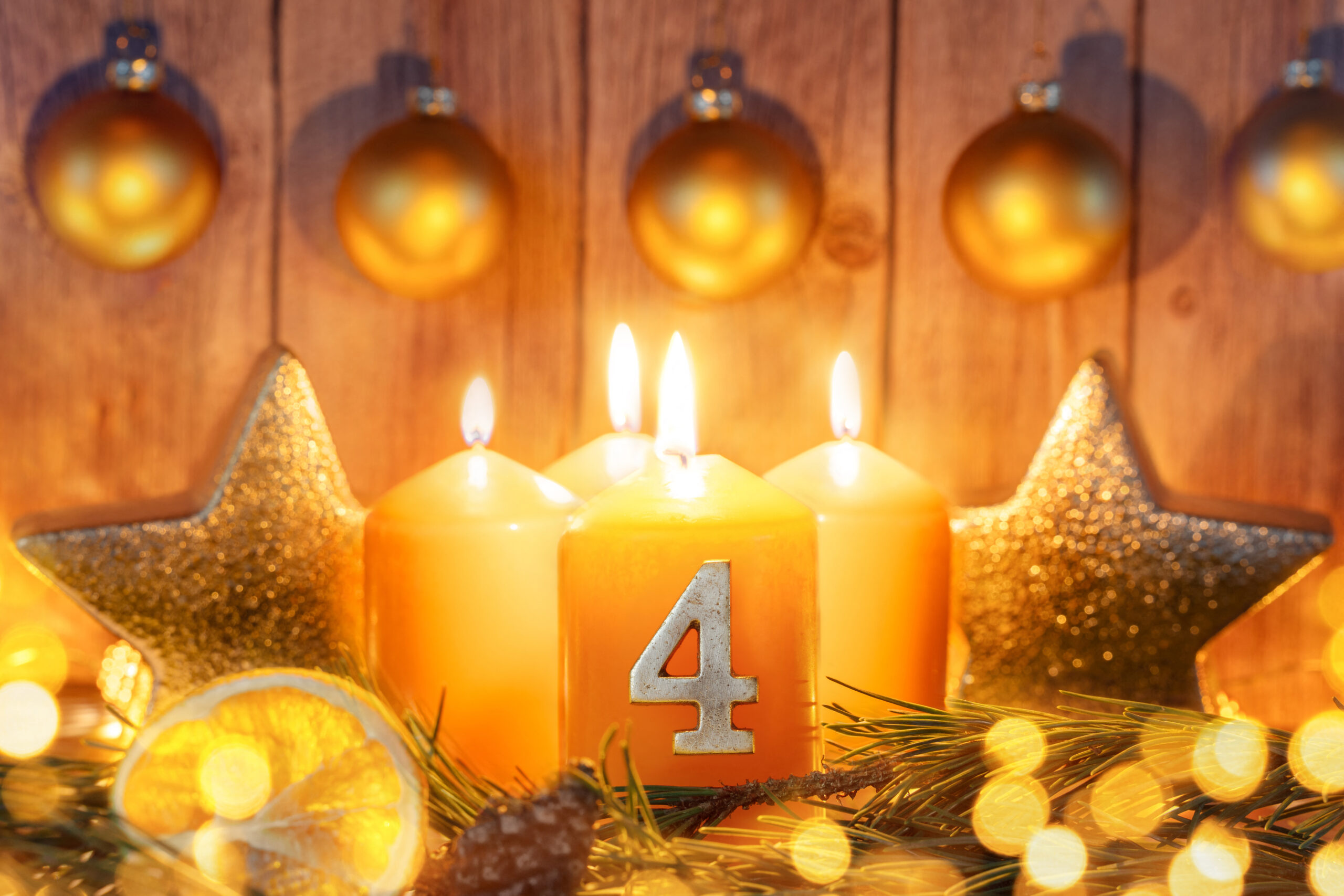 vier leuchtende adventskerzen zum 4. advent mit goldenen kugeln, sternen und weihnachtlicher dekoration
