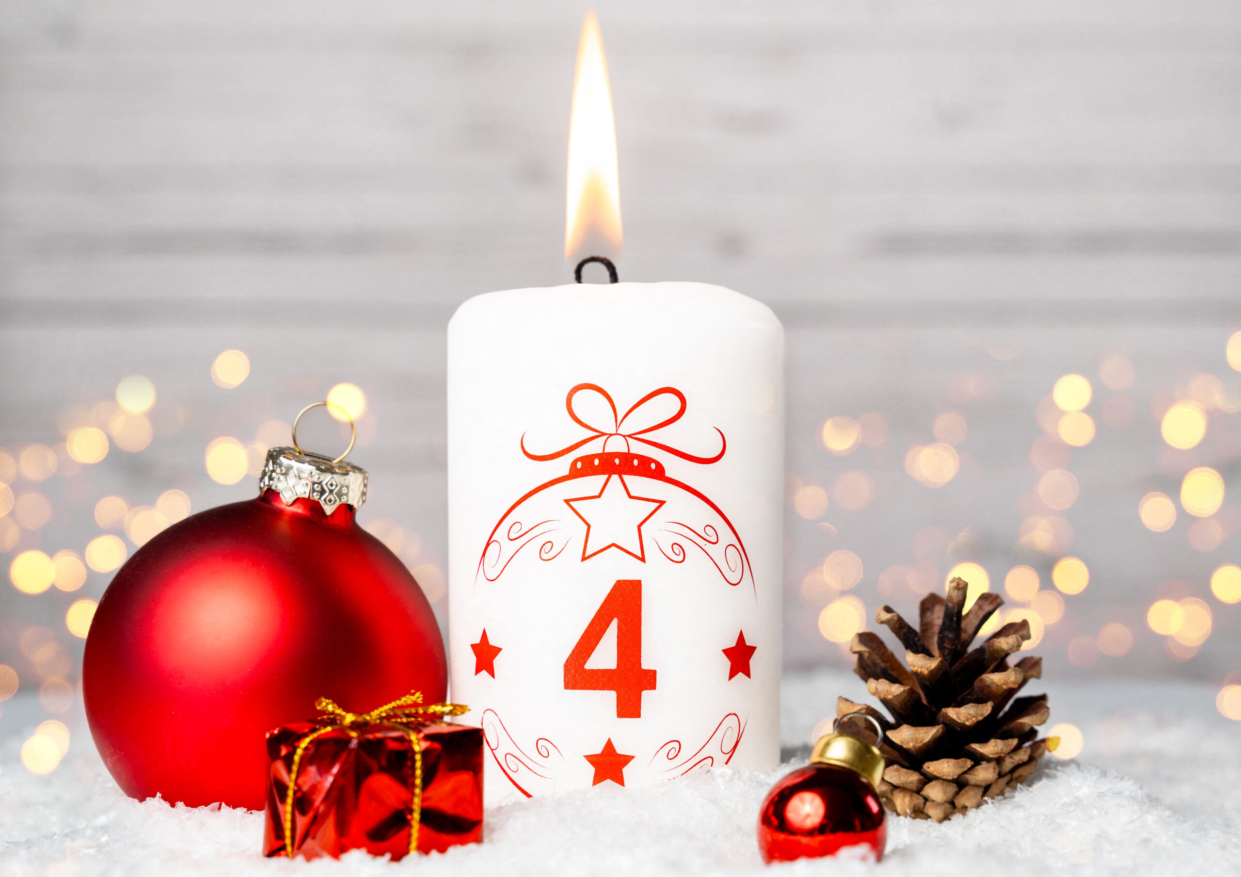 weiße kerze mit zahl 4 zum 4. adventsabend, umgeben von roter weihnachtskugel, tannenzapfen und winterlicher adventsdeko im schnee