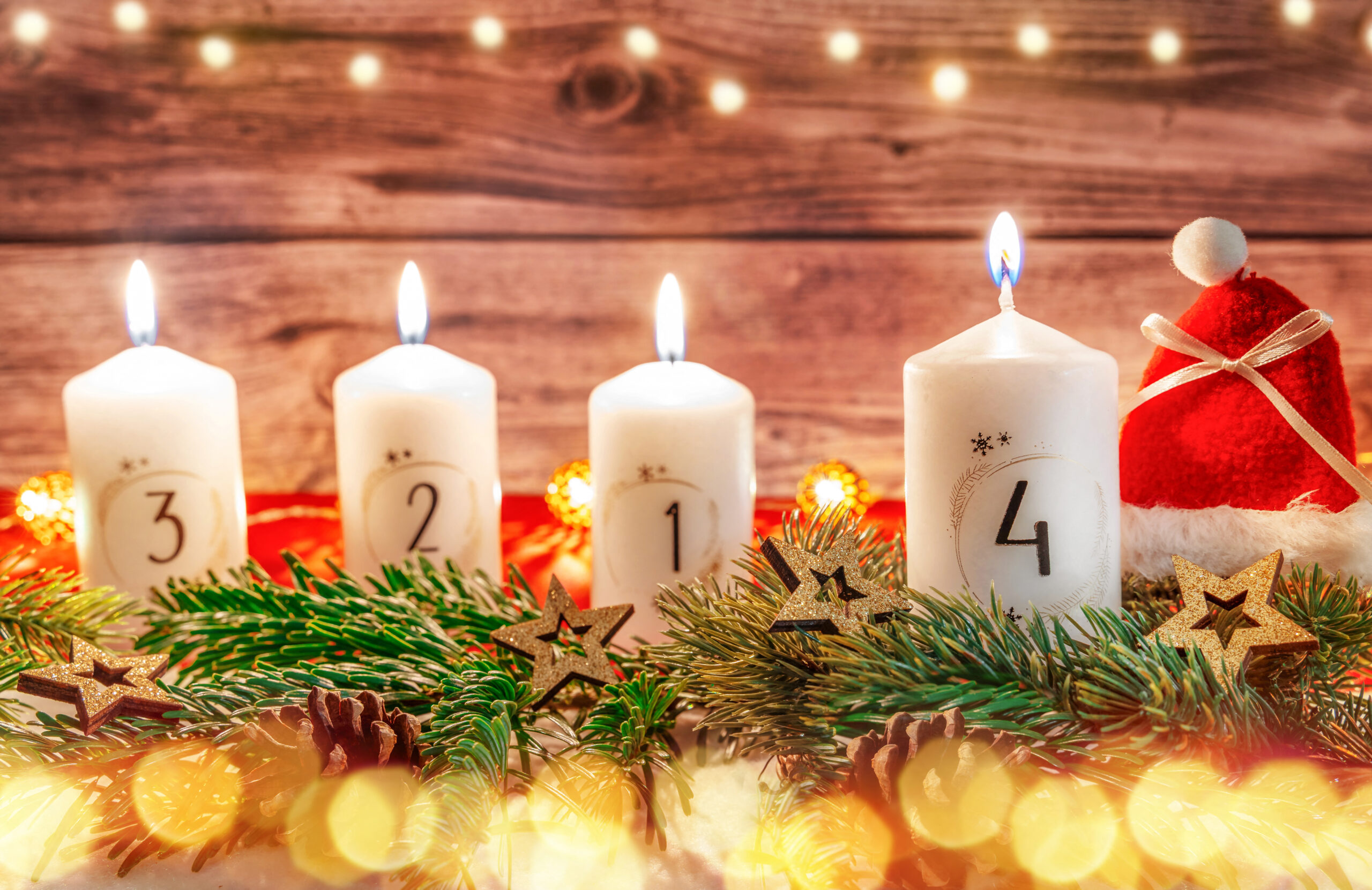 vier weiße kerzen zum 4. adventssonntag, die kerze für den 4. advent brennt, dekoriert mit tannenzweigen, sternen und weihnachtsmütze