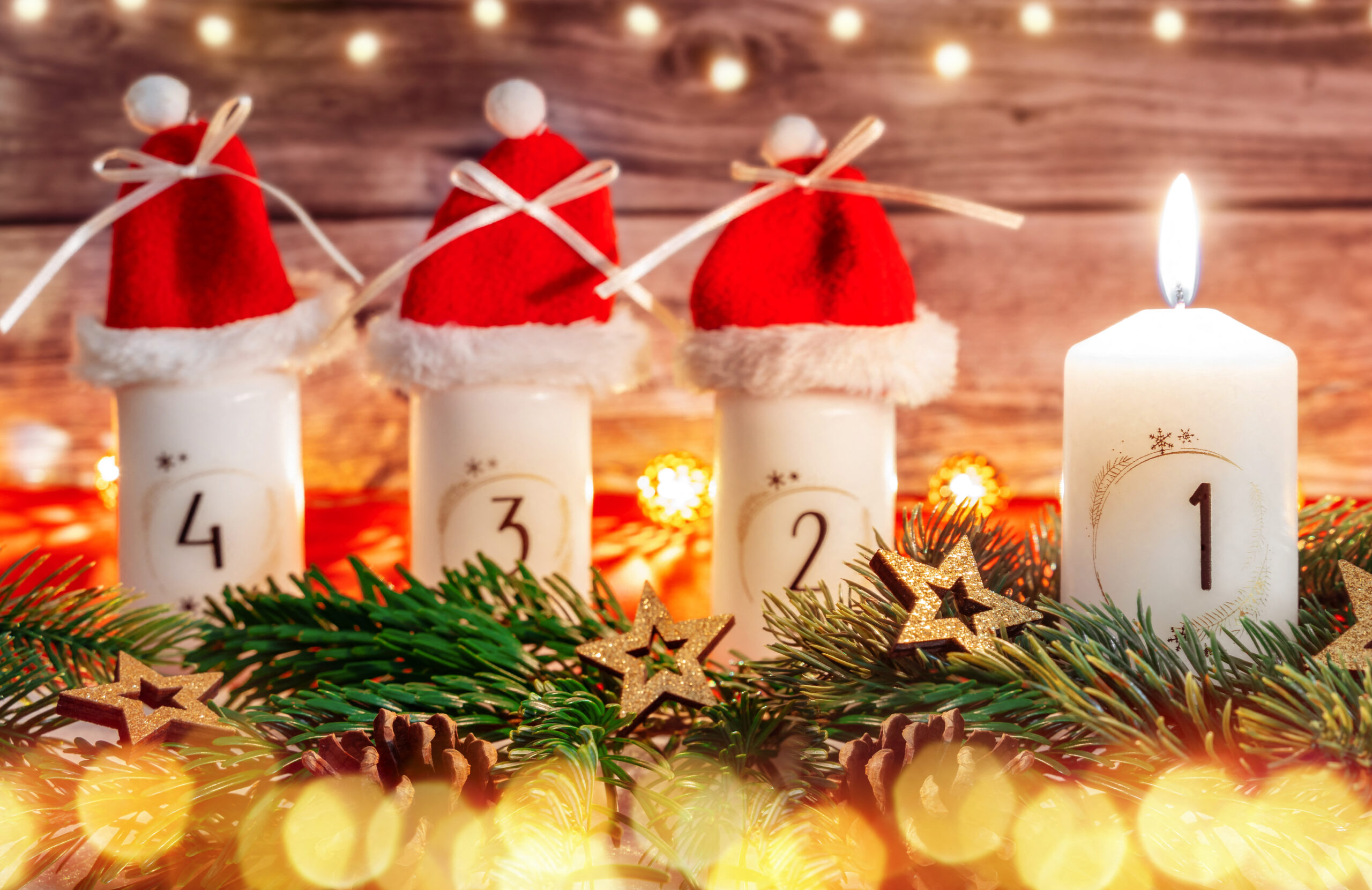 lustiges 1 advent bild mit weißer adventskerze, kleinen weihnachtsmützen und tannenzweigen