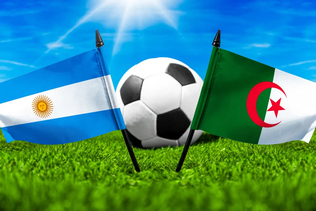 Argentinische und algerische Flagge mit Fußball auf grünem Rasen unter blauem Himmel.