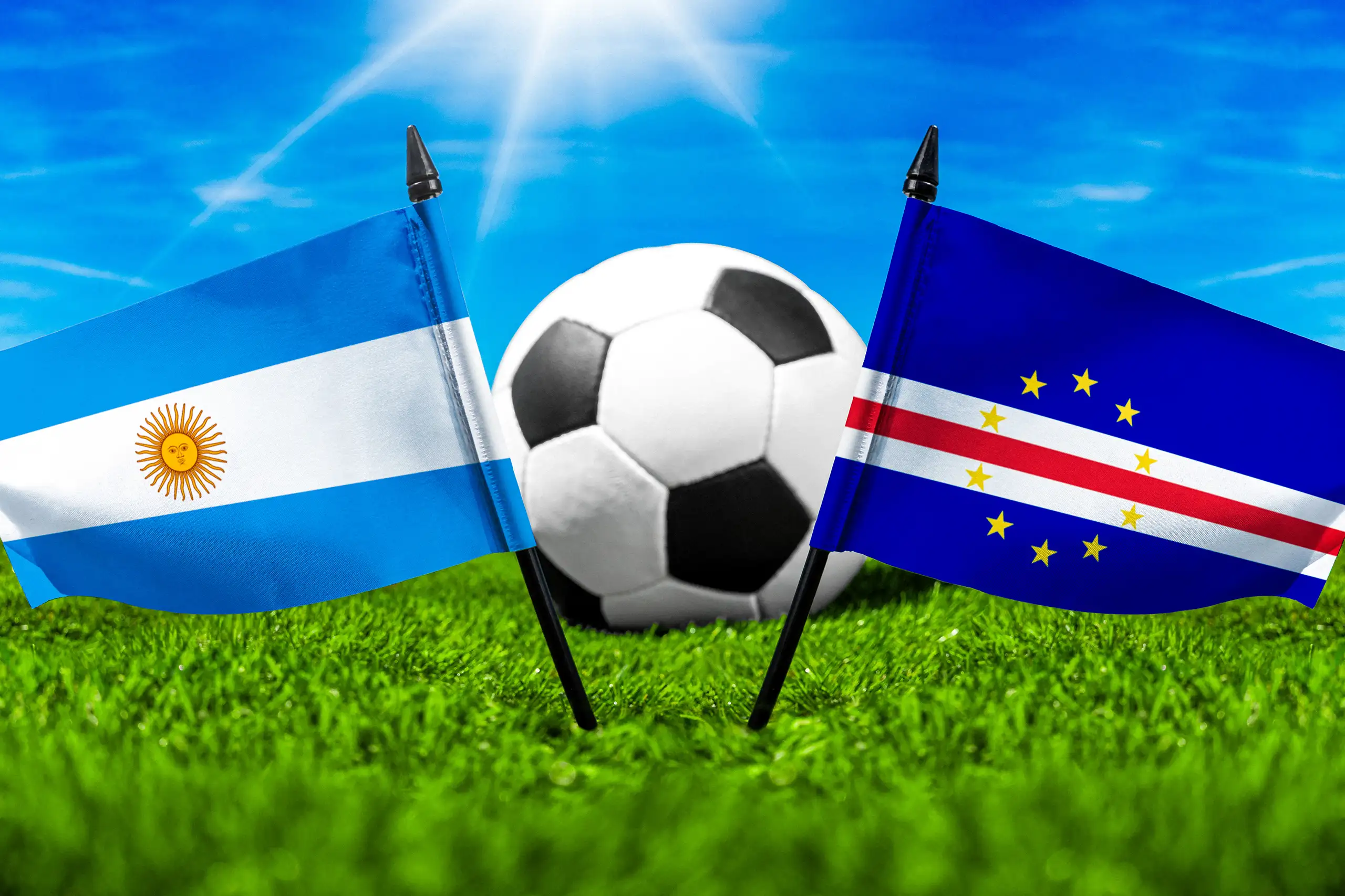 nationalflaggen von argentinien und kap verde mit fußball auf grünem rasen vor blauem himmel.
