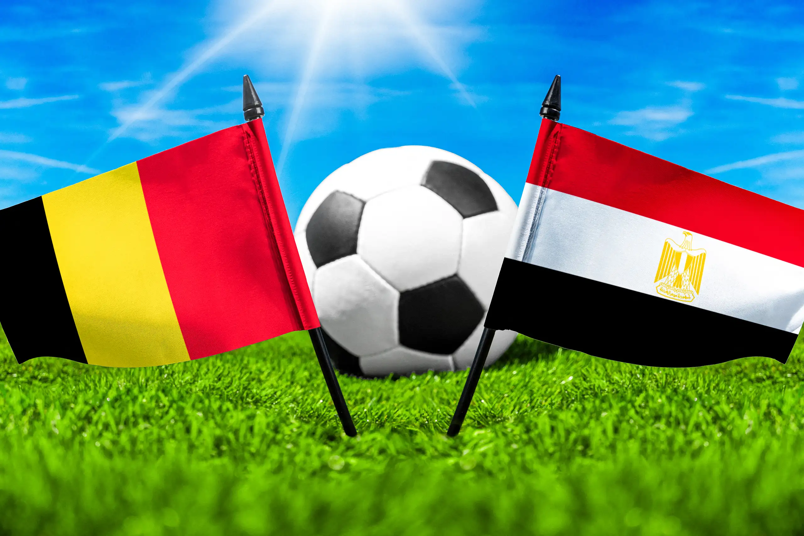 flaggen von belgien und ägypten mit fußball auf grünem rasen unter blauem himmel.