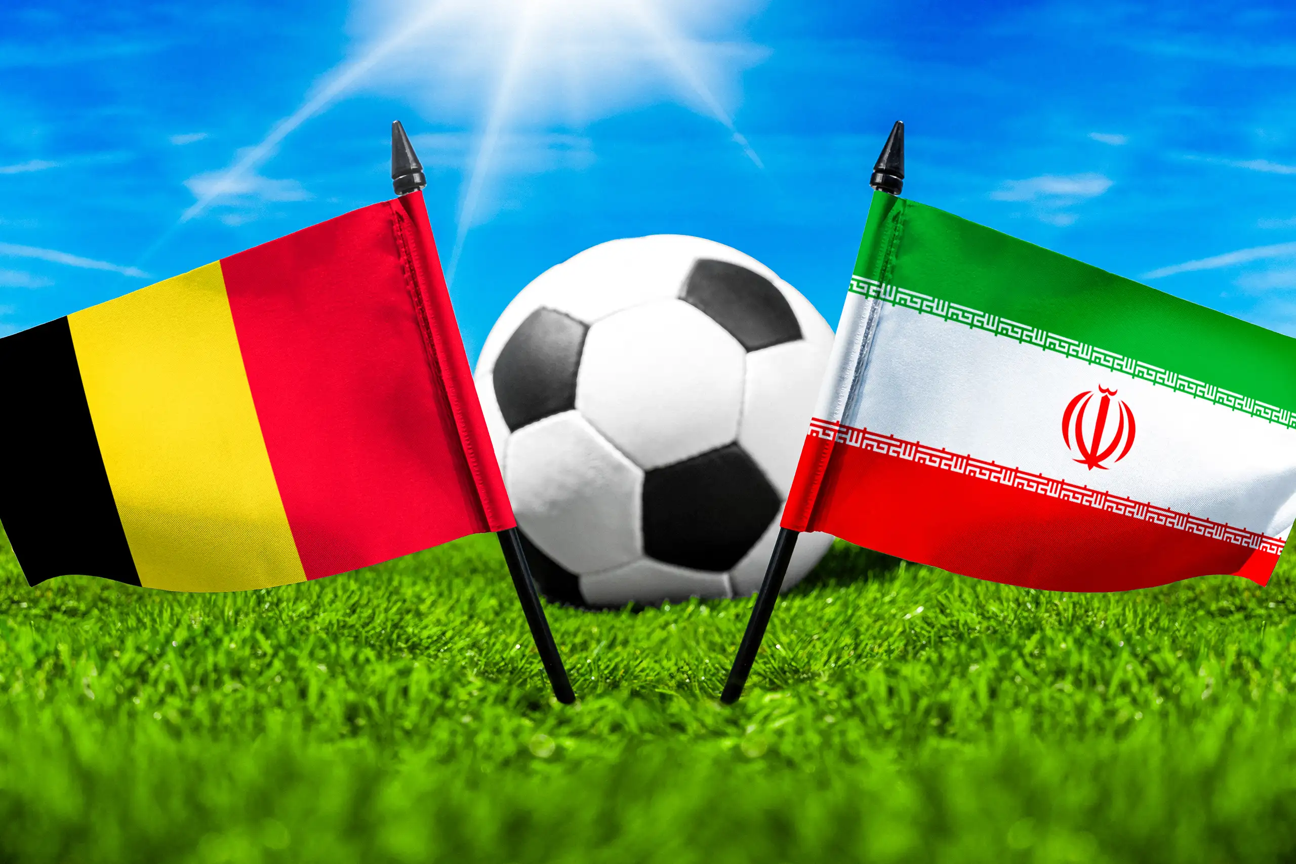belgische und iranische flagge vor einem fußball auf grünem rasen bei einem internationalen fußballspiel.