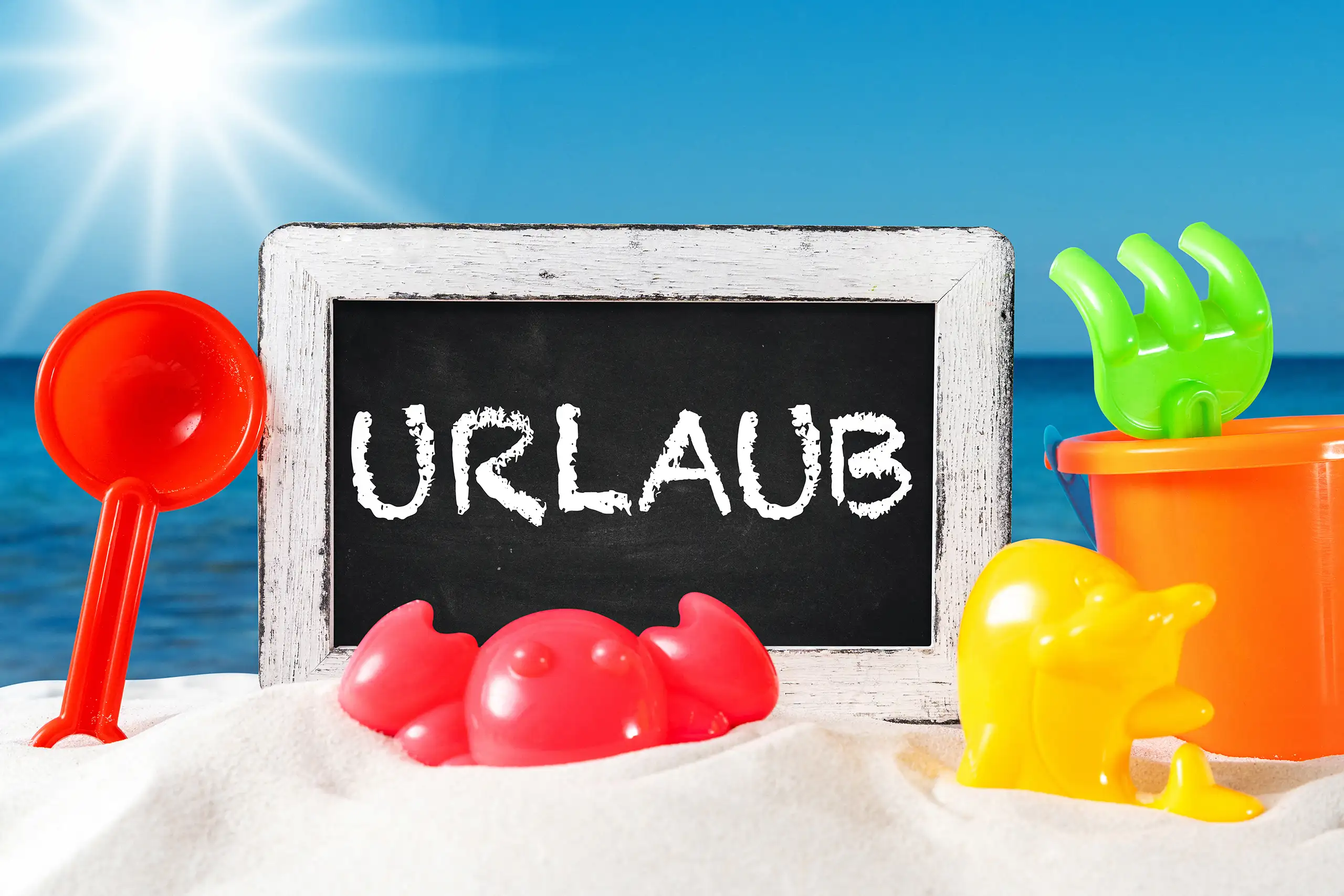 Urlaub Bild mit schwarzer Kreidetafel, buntem Strandspielzeug, Sand und blauem Meer