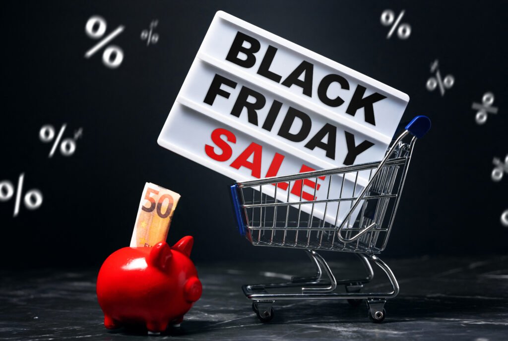 Black Friday Sale – Einkaufswagen mit Schild und rotem Sparschwein vor dunklem Hintergrund