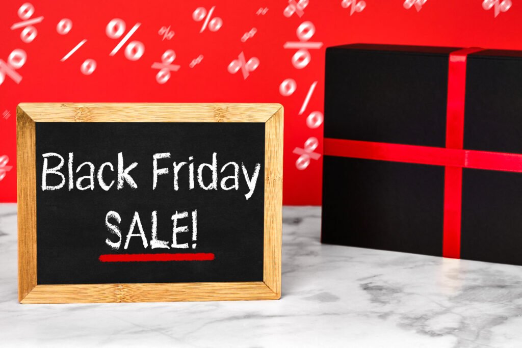 Black Friday Sale Schild – schwarze Tafel mit weißem Schriftzug und rotem Unterstrich neben Geschenk mit Schleife