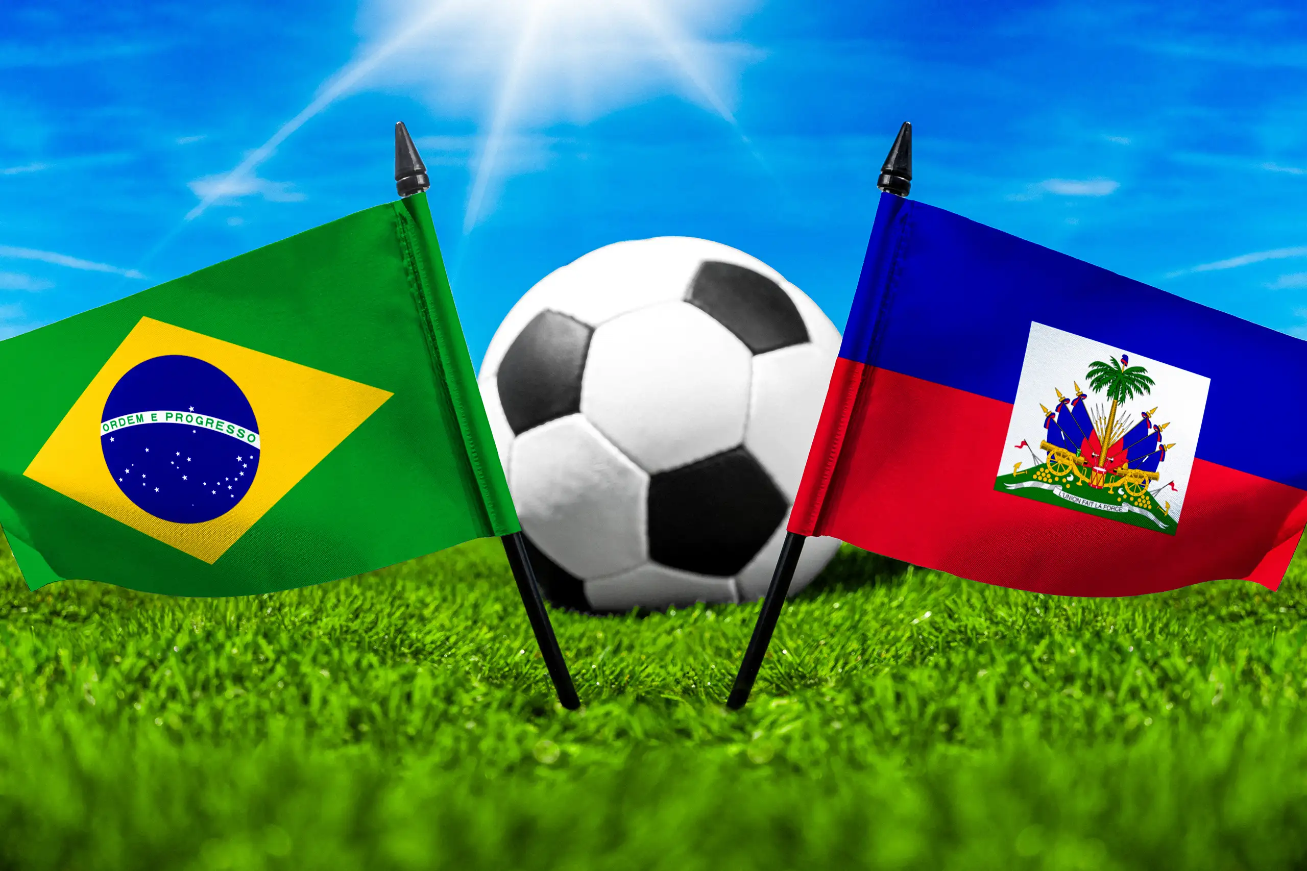 brasilianische und haitianische flagge vor einem fußball auf grünem rasen unter blauem himmel.