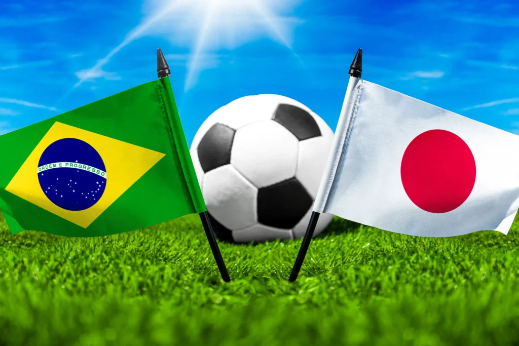 Brasilien gegen Japan mit Nationalflaggen und Fußball auf grünem Rasen bei einer internationalen Fußballbegegnung.