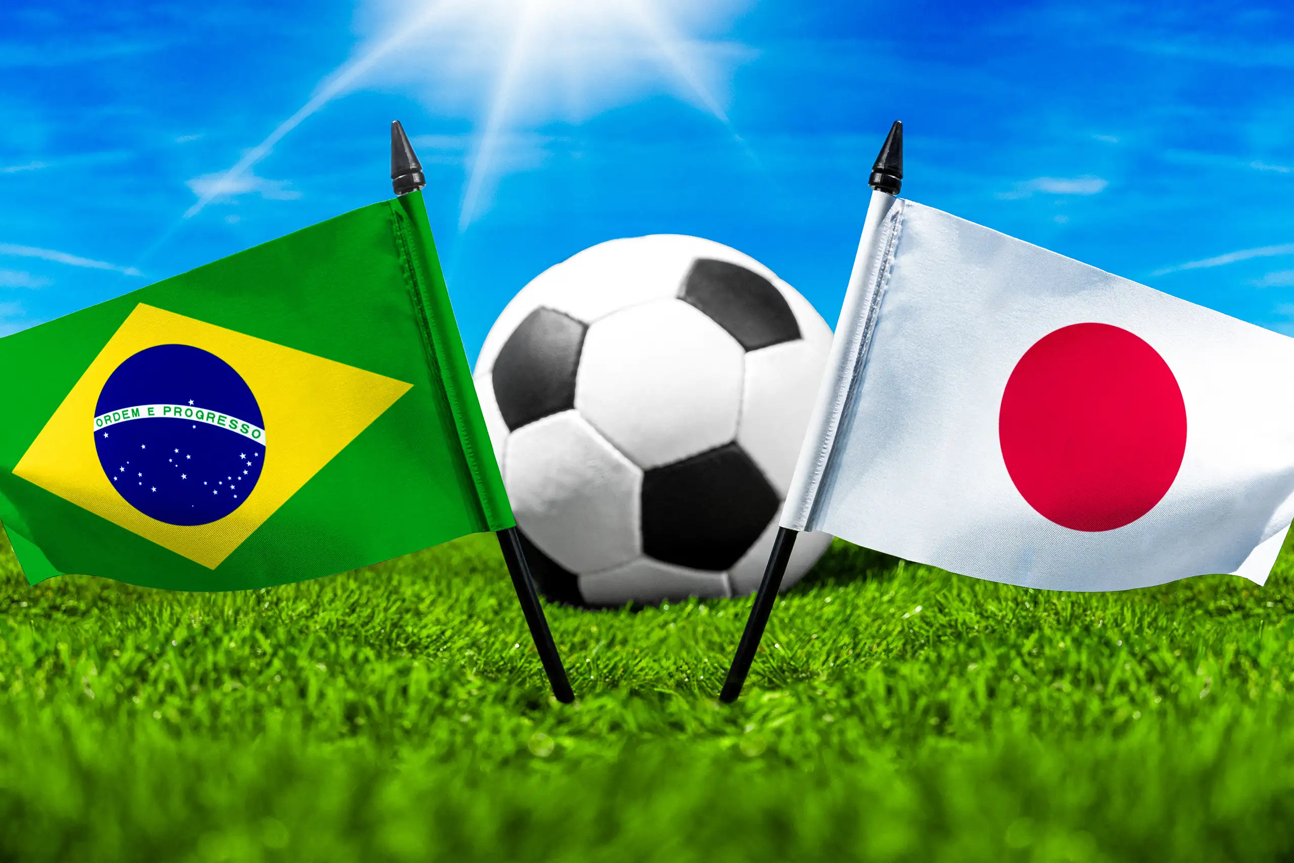 brasilien gegen japan mit nationalflaggen und fußball auf grünem rasen bei einer internationalen fußballbegegnung.