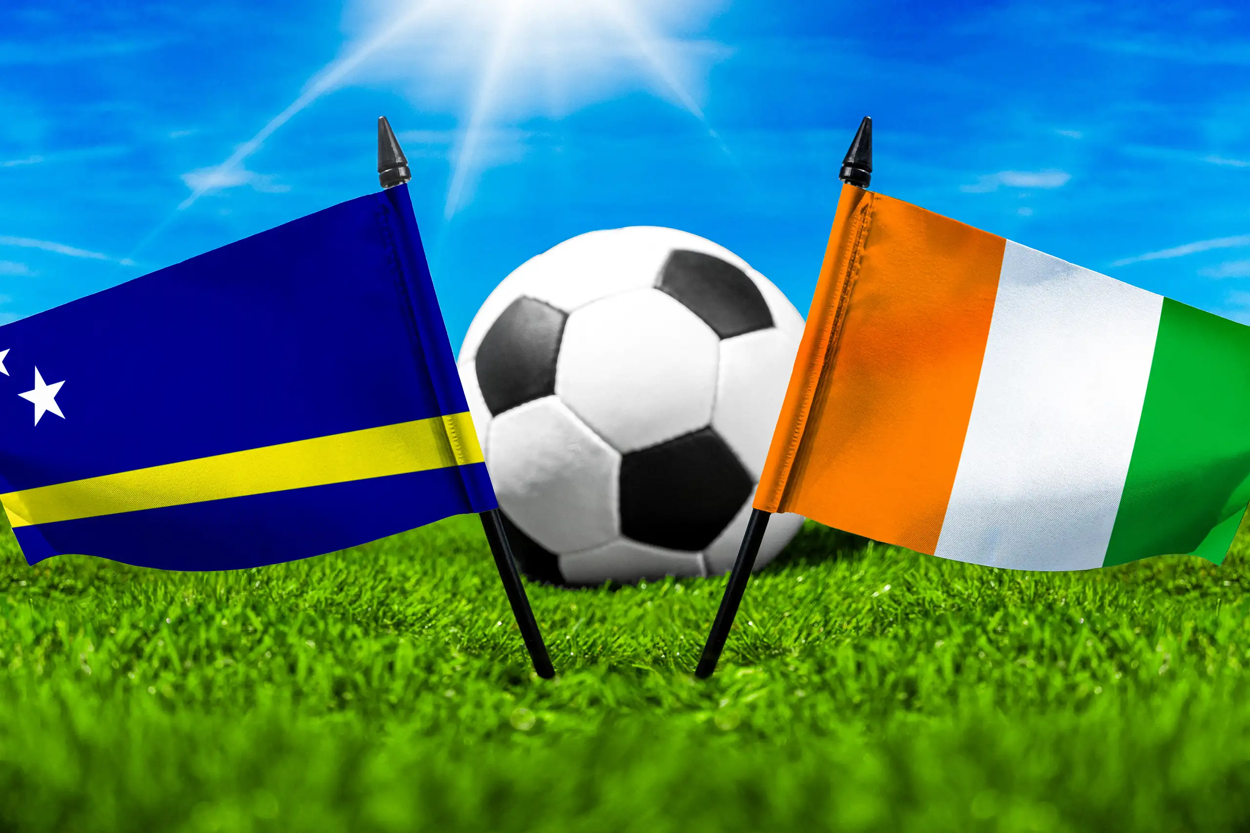 flaggen von curaçao und der elfenbeinküste mit fußball auf grünem rasen unter blauem himmel.
