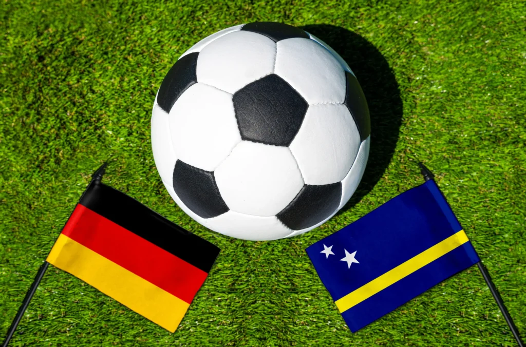 Fußball auf Rasen zwischen den Nationalflaggen von Deutschland und Curaçao bei einem internationalen Fußballspiel.
