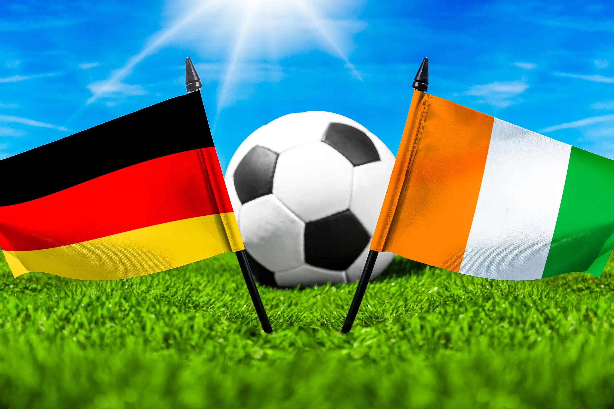 fußball zwischen den nationalflaggen von deutschland und elfenbeinküste auf grünem spielfeldrasen.