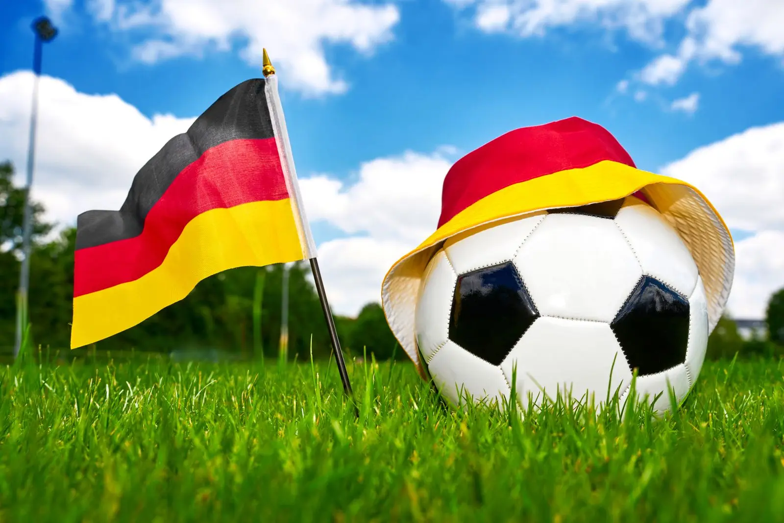 deutschlandflagge neben fußball mit schwarz-rot-gelbem fanhut auf grünem rasen.