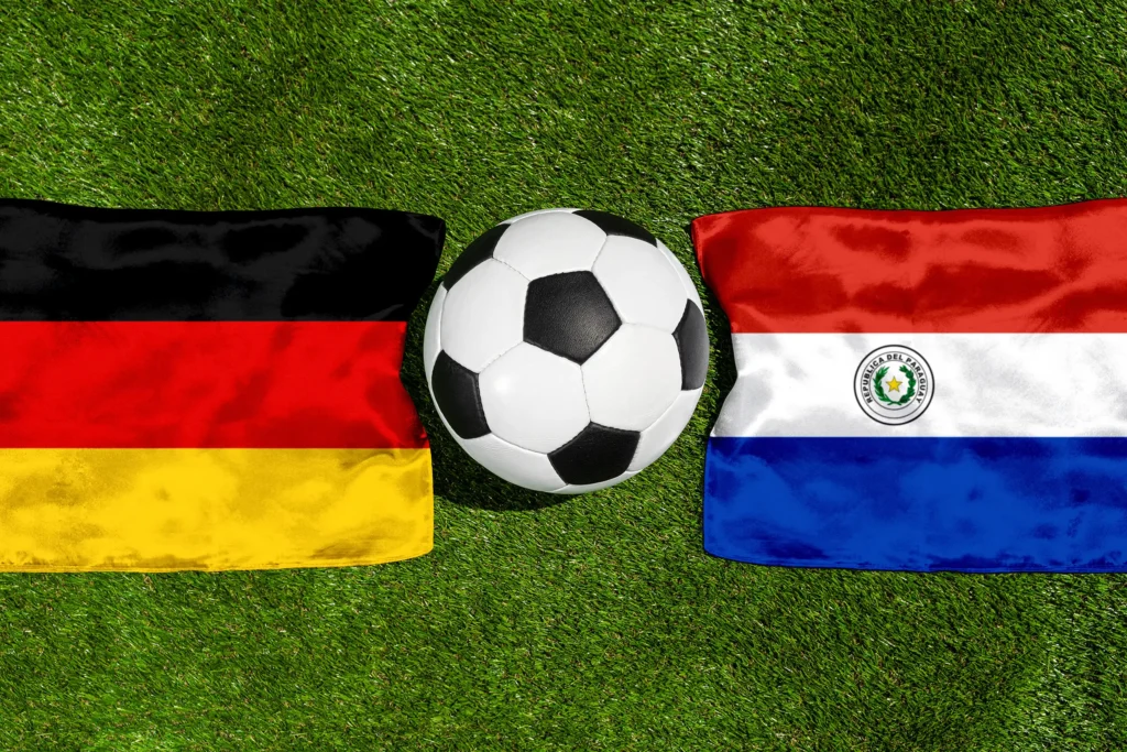 Flaggen von Deutschland und Paraguay mit einem Fußball auf grünem Rasen als Motiv für ein internationales Fußball-Länderspiel.