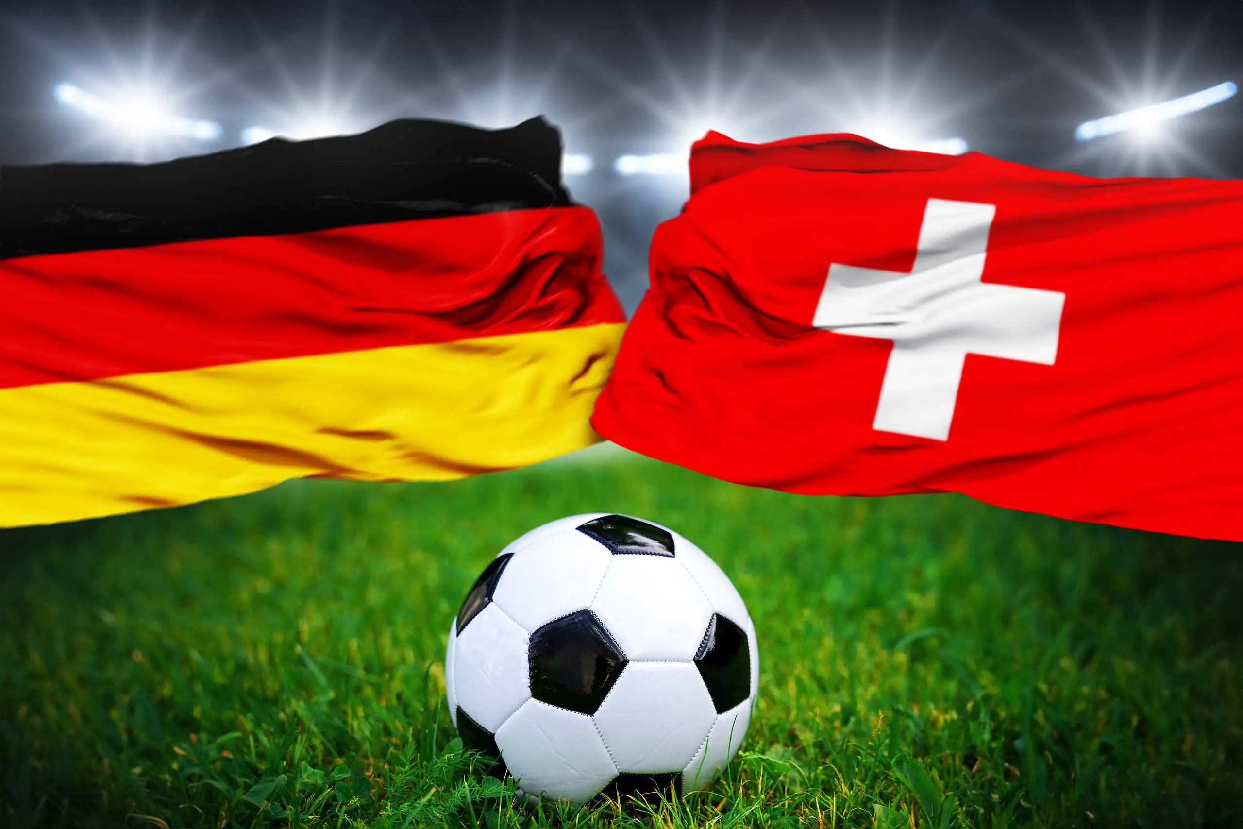 deutschland- und schweiz-flagge vor stadionbeleuchtung mit fußball auf grünem rasen.