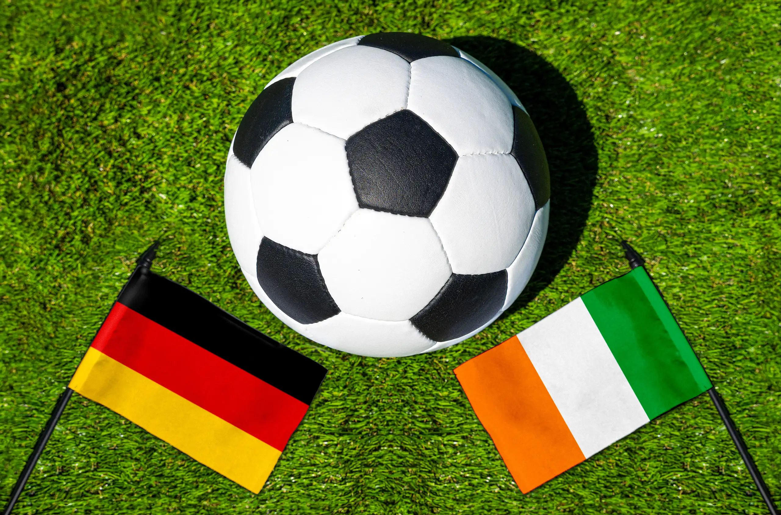 fußball zwischen den nationalflaggen von deutschland und elfenbeinküste auf grünem rasen.