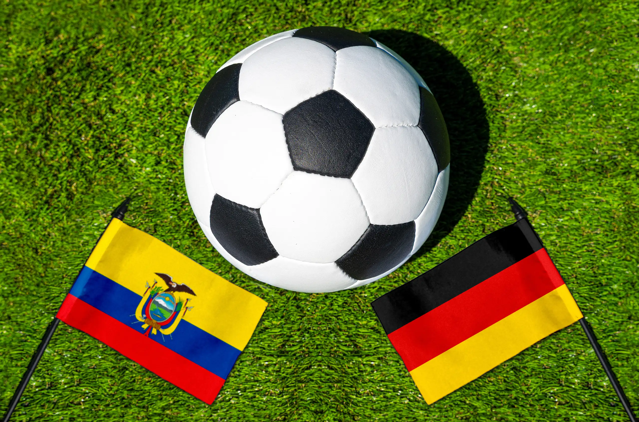 ecuador deutschland fußballspiel mit fußball zwischen den nationalflaggen von ecuador und deutschland auf grünem rasen.