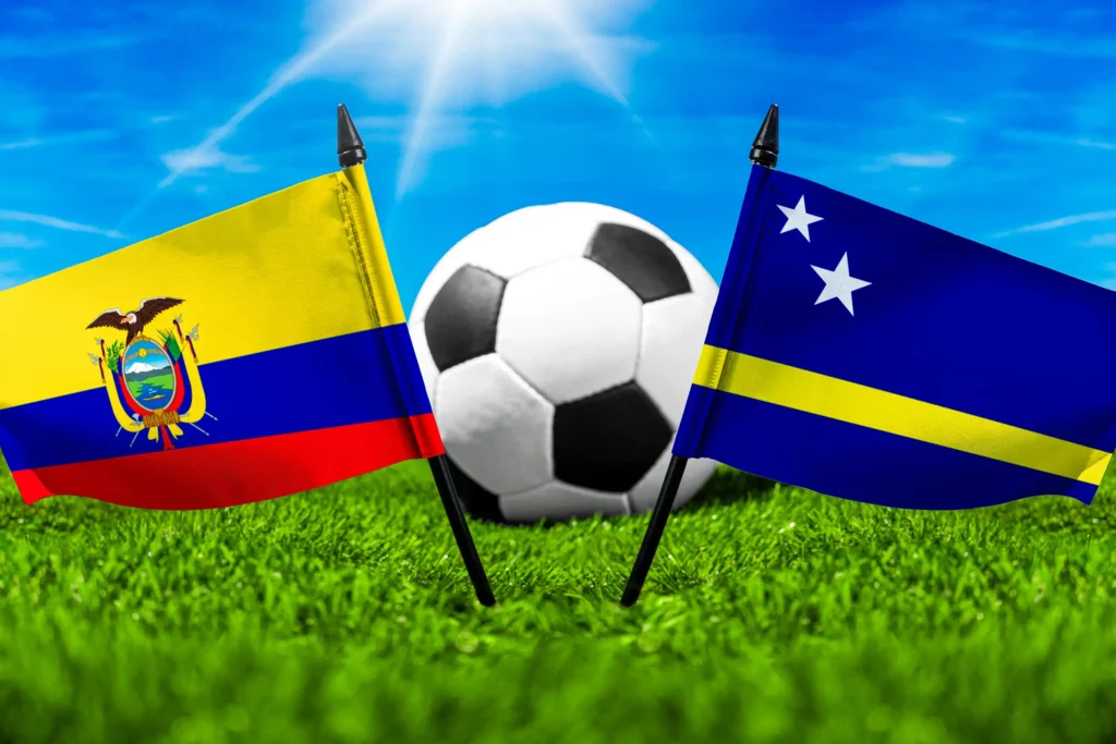 Flaggen von Ecuador und Curaçao mit Fußball auf Rasen unter blauem Himmel.