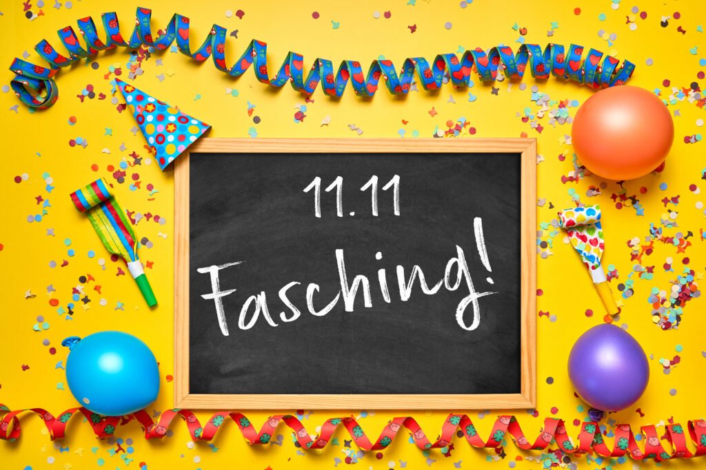 Faschingsanfang Bilder – schwarze Tafel mit Aufschrift „11.11 Fasching!“ auf gelbem Hintergrund mit Luftschlangen, Ballons und Konfetti.