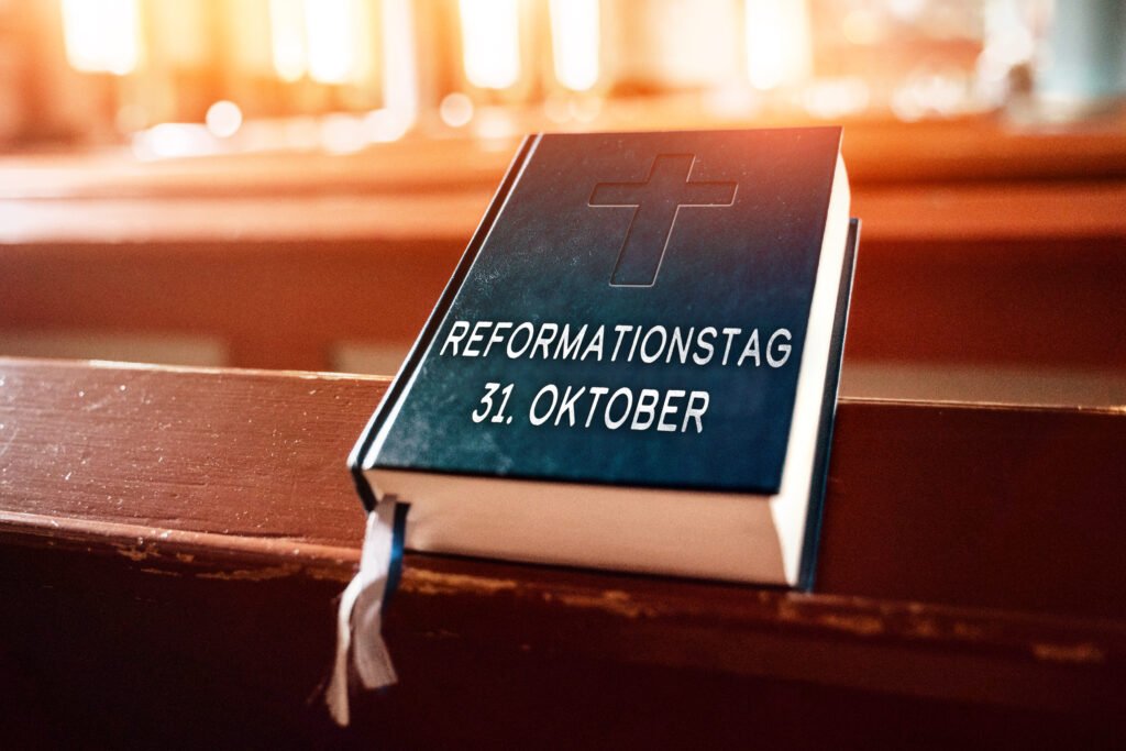Bibel mit Kreuzprägung und Aufschrift Reformationstag 31. Oktober liegt auf einer hölzernen Kirchenbank im warmen Sonnenlicht.