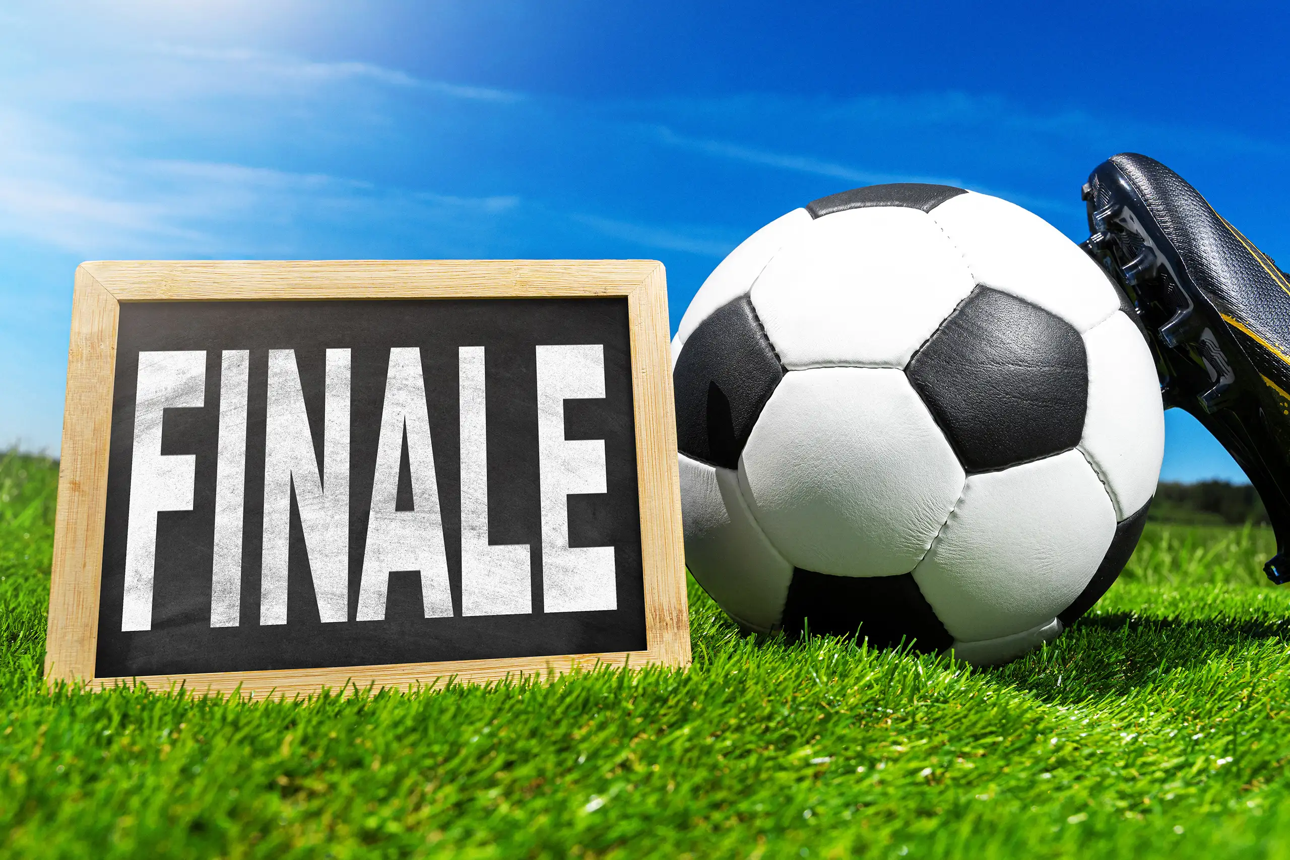 tafel mit der aufschrift finale neben fußball und fußballschuh auf grünem rasen.