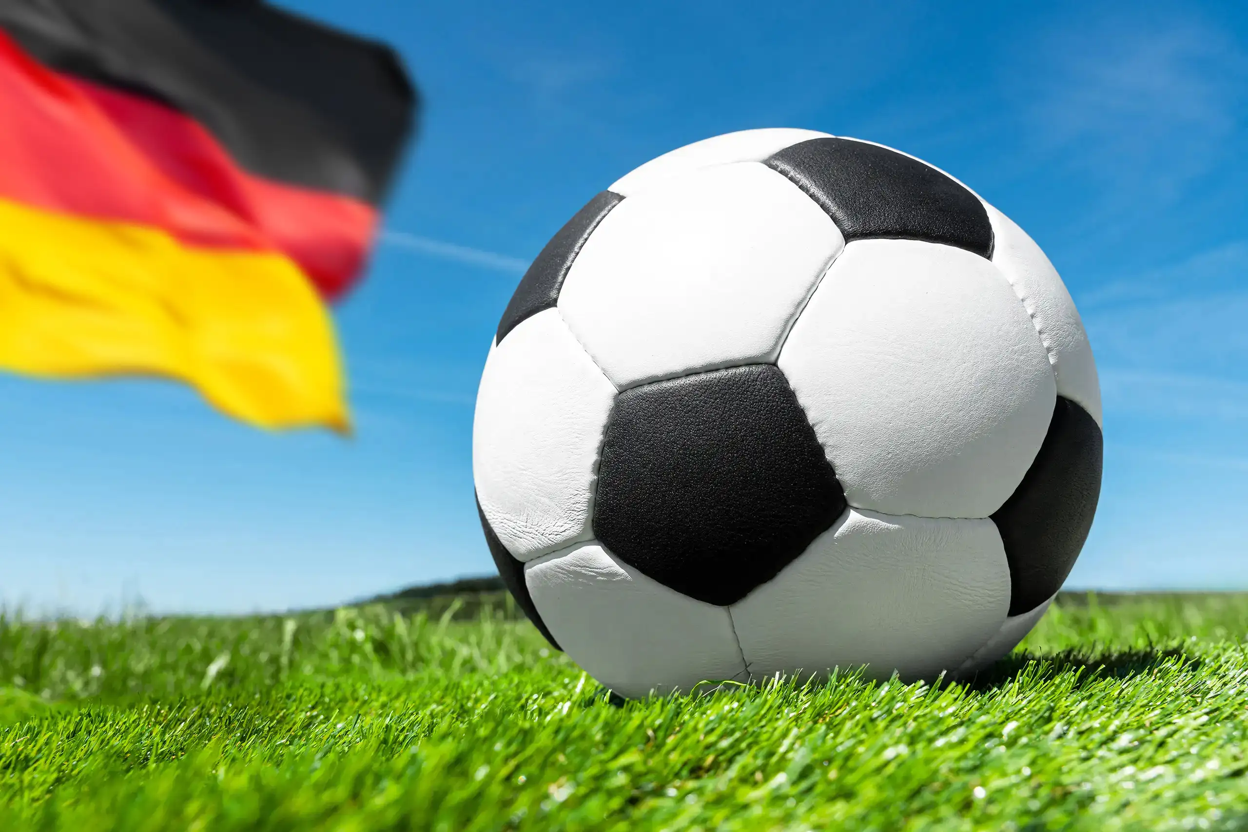 fußball auf grünem spielfeldrasen mit deutschland fahne im hintergrund.