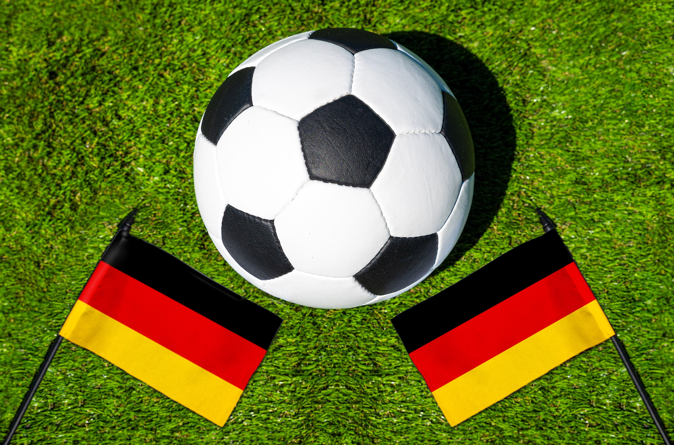 fußball auf rasen mit zwei deutschlandfahnen in schwarz-rot-gold aus der vogelperspektive.
