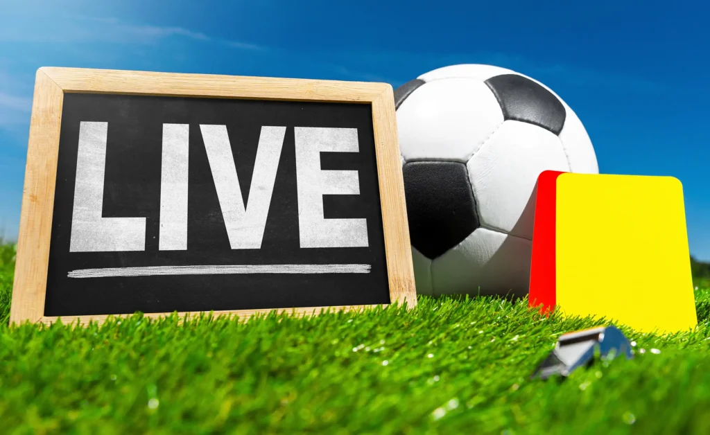 Fußball live mit Ball, gelber Karte, roter Karte und Schiedsrichterpfeife auf grünem Spielfeldrasen.
