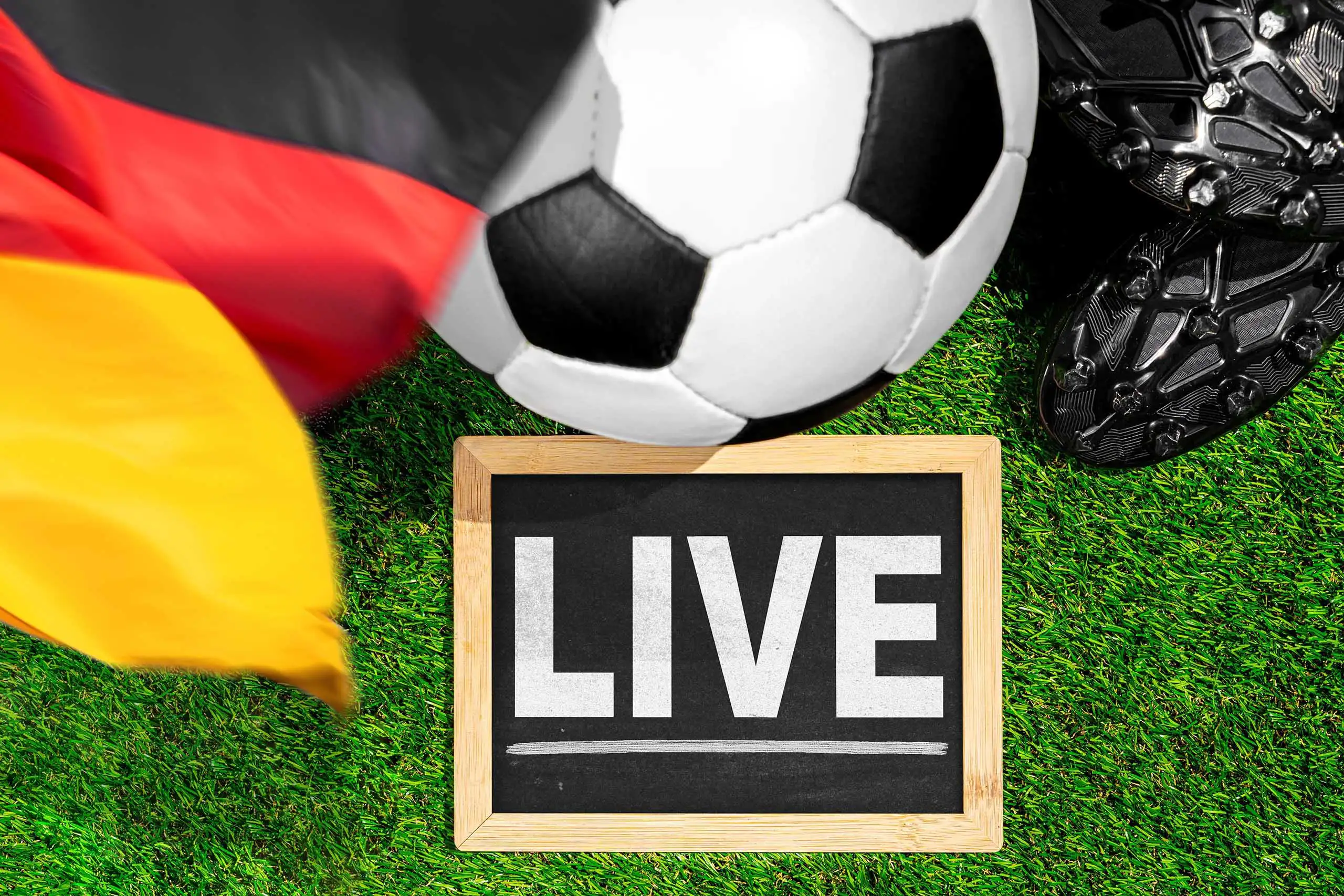 fußball mit live-hinweis, deutschland fahne und fußballschuhen auf grünem spielfeldrasen.