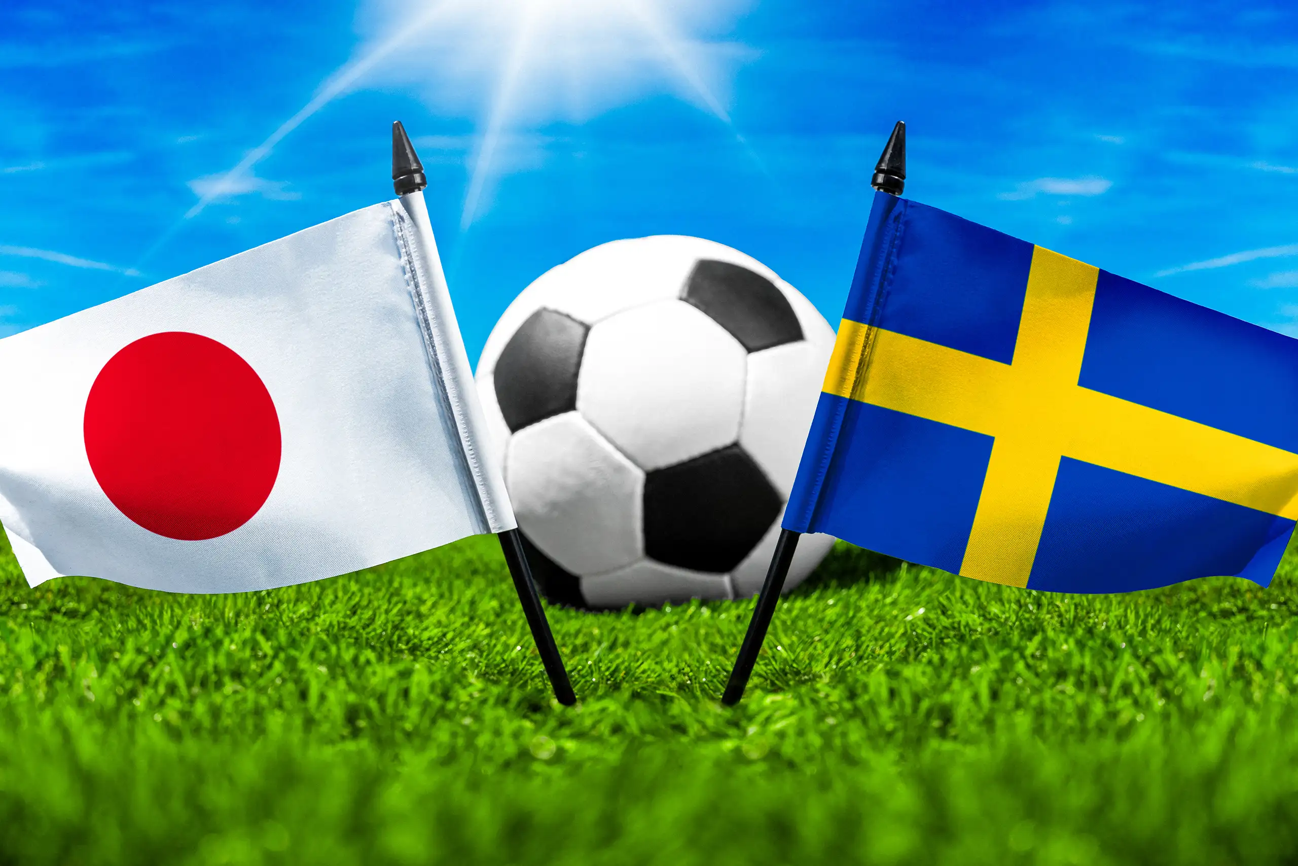 flaggen von japan und schweden mit fußball auf grünem rasen unter blauem himmel.