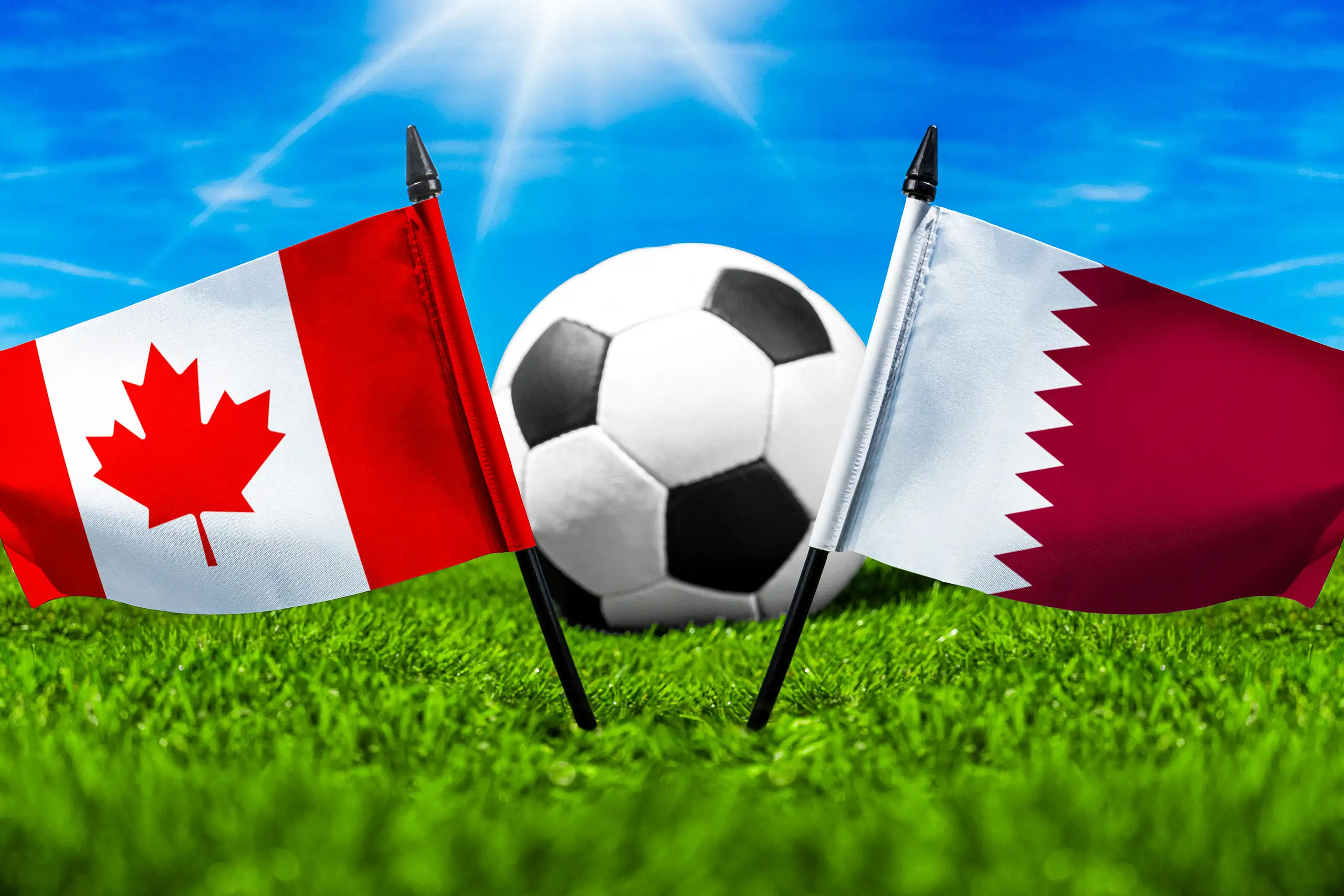 flaggen von kanada und katar mit fußball auf grünem rasen unter blauem himmel.