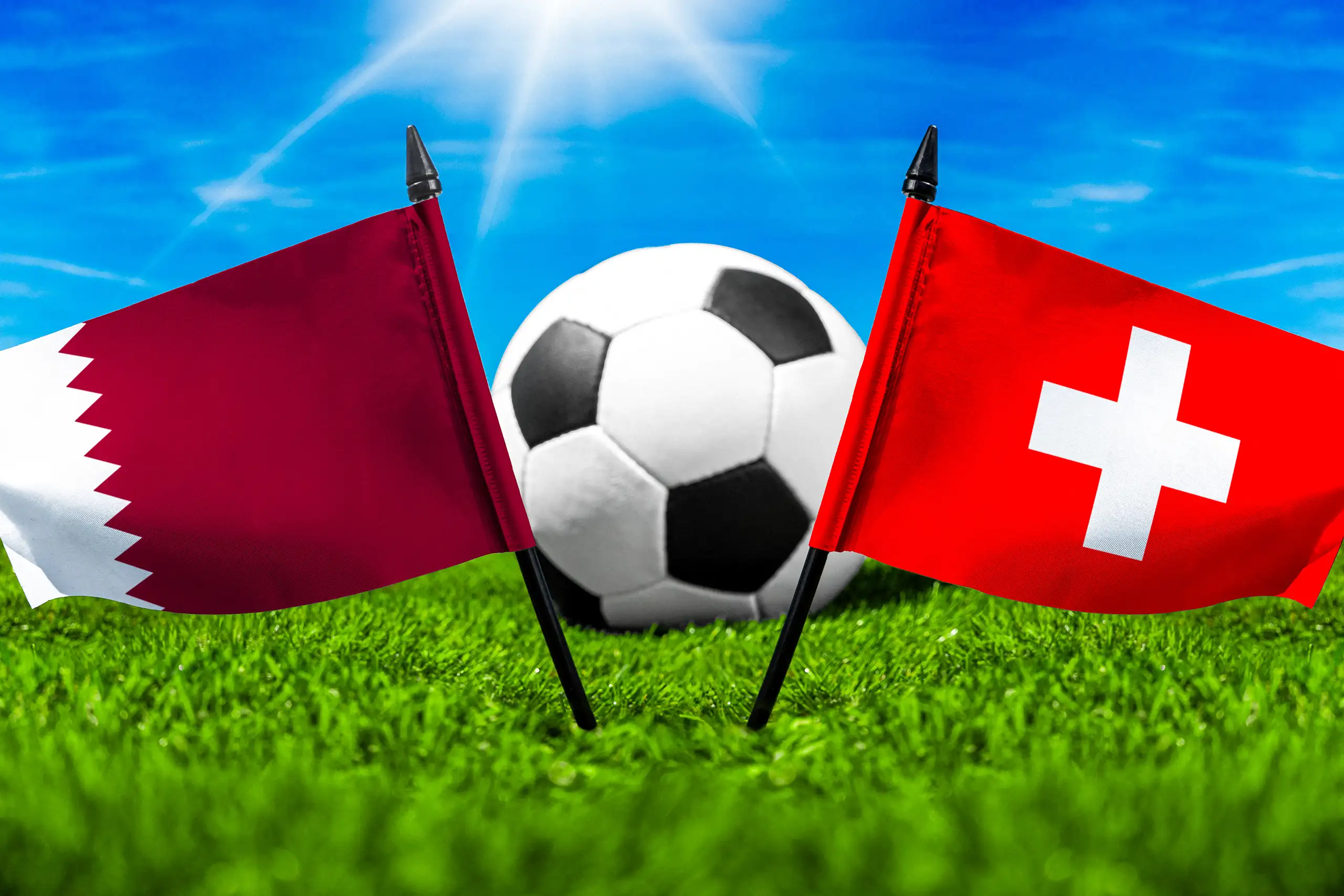 nationalflaggen von katar und der schweiz vor einem fußball auf grünem rasen unter blauem himmel.