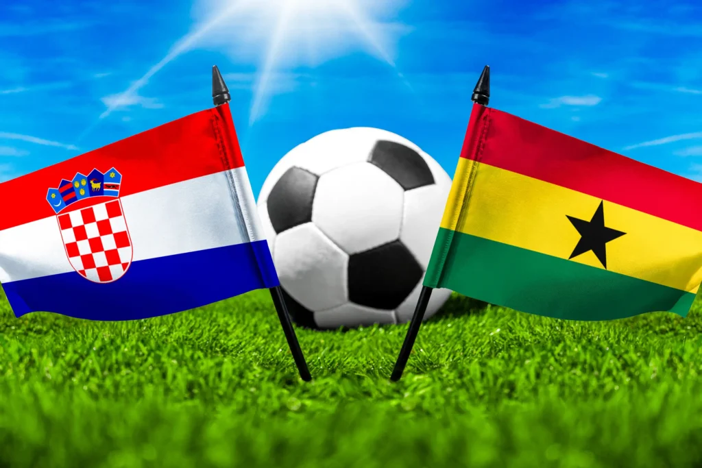 Kroatien gegen Ghana mit Fußball auf Rasen und den Nationalflaggen beider Länder unter blauem Himmel.