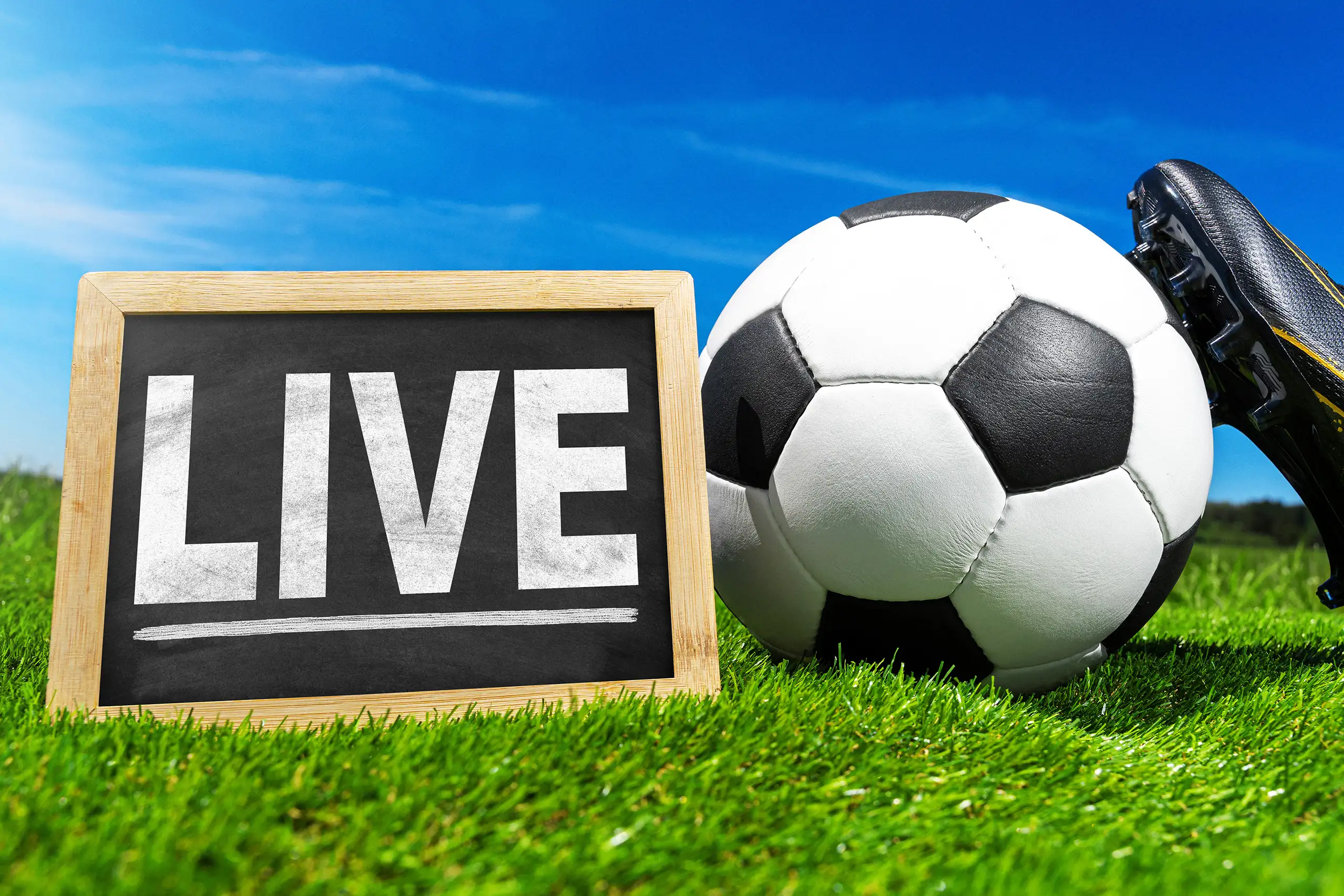 live-tafel neben fußball und fußballschuh auf grünem rasen unter blauem himmel.