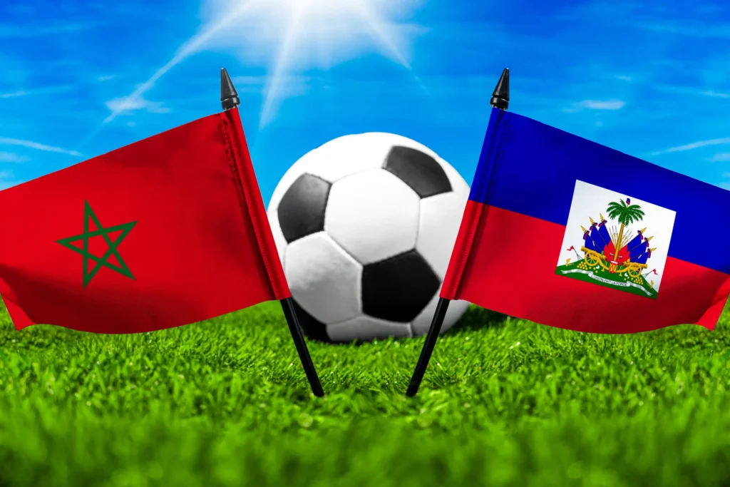 Marokko gegen Haiti mit Fußball auf Rasen und den Nationalflaggen beider Länder unter blauem Himmel.