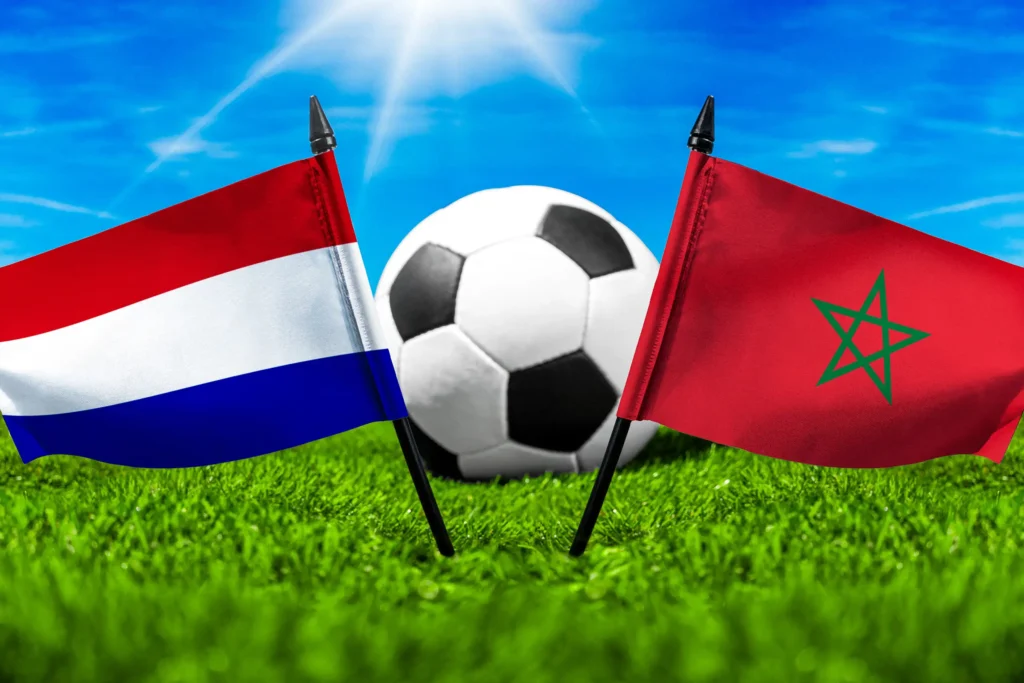 Niederlande gegen Marokko mit Nationalflaggen und Fußball auf grünem Rasen bei einer internationalen Fußballbegegnung.