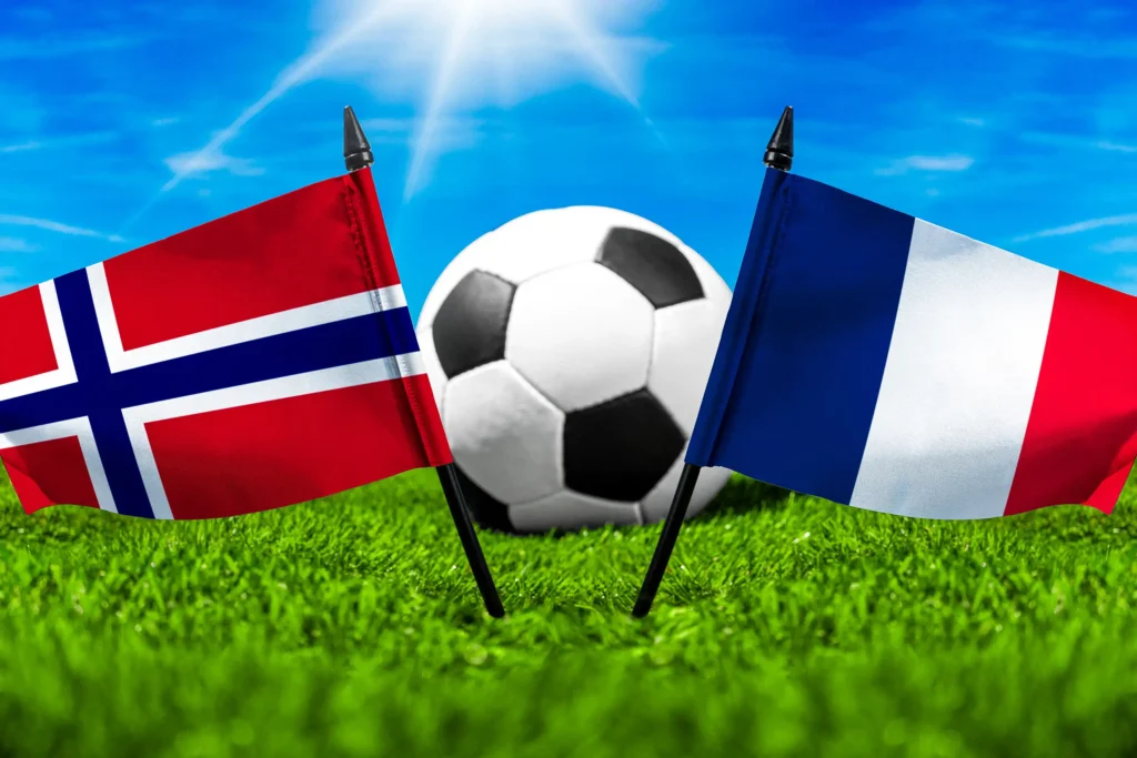 Nationalflaggen von Norwegen und Frankreich vor einem Fußball auf grünem Rasen unter blauem Himmel.