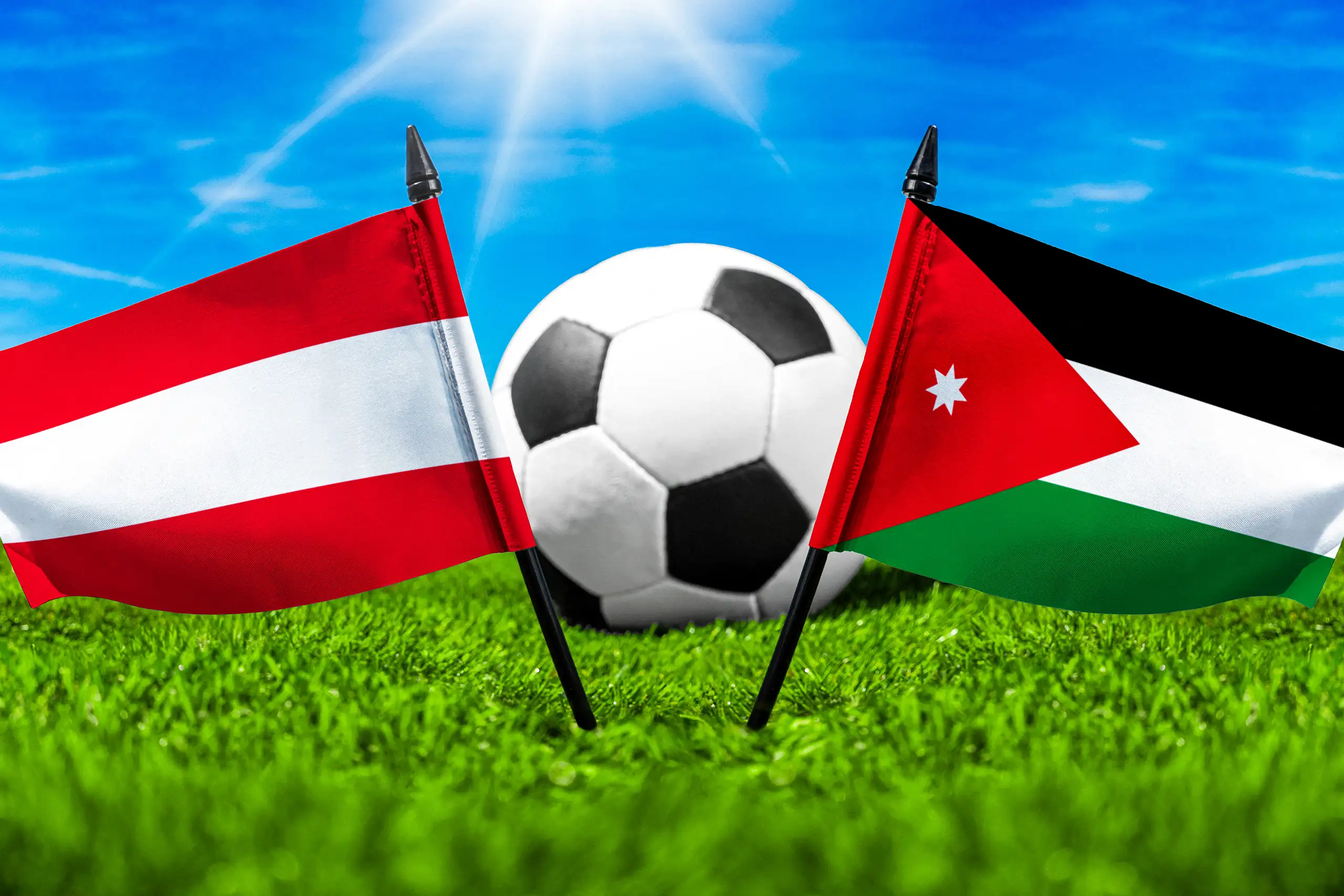 österreich jordanien fußballspiel mit fußball zwischen österreichischer und jordanischer nationalflagge auf grünem spielfeldrasen.