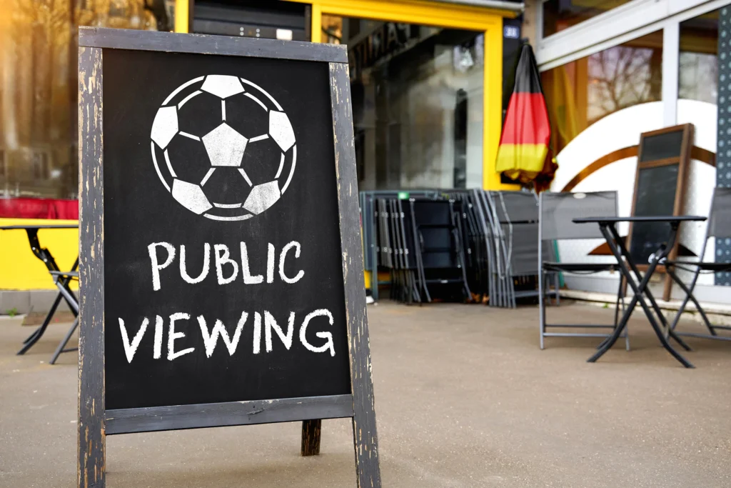 Public Viewing vor einem Restaurant mit Werbetafel, Sitzplätzen und Deutschlandflagge.