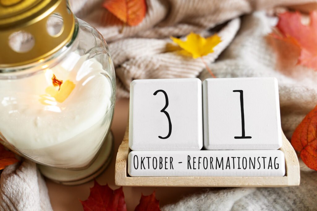 Reformationstag mit brennender Kerze in Glaslaterne, Holzkalender mit Datum 31. Oktober und buntem Herbstlaub auf weicher Decke.