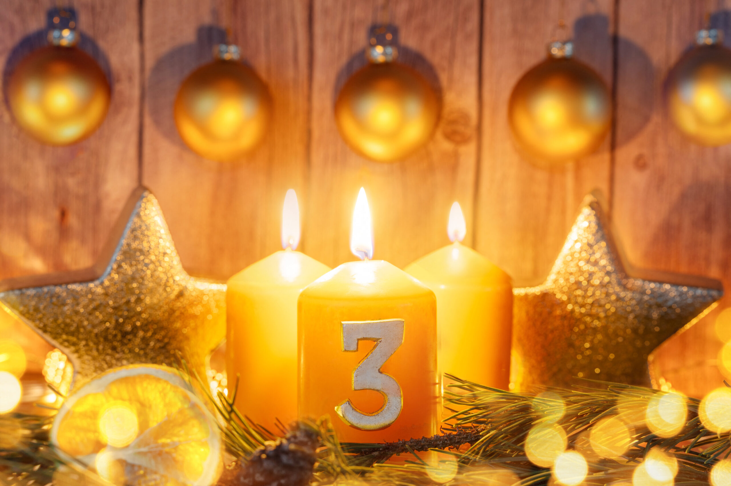 3 advent mit drei brennenden kerzen und goldener weihnachtsdeko vor holzhintergrund