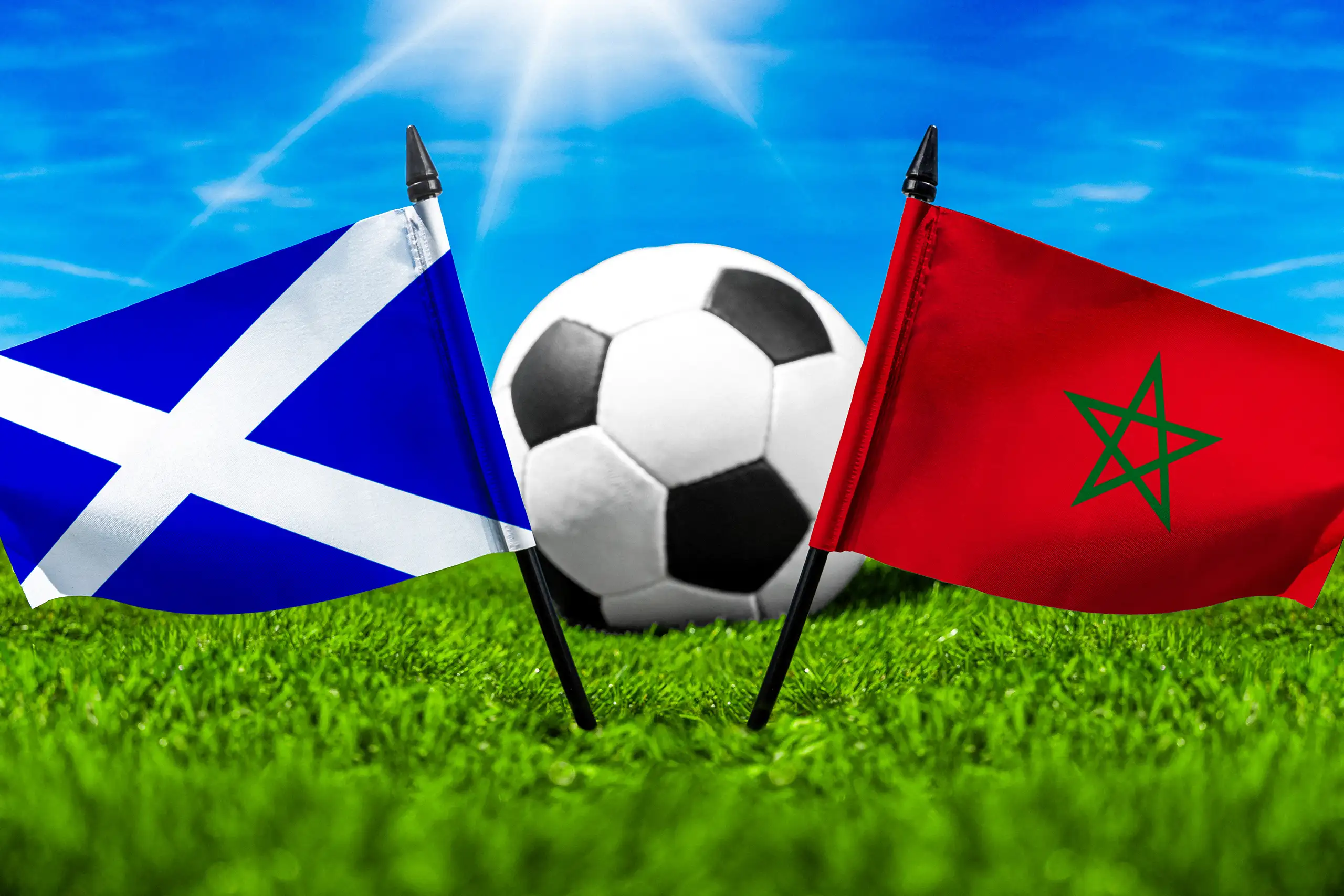 flaggen von schottland und marokko mit fußball auf grünem rasen unter blauem himmel.