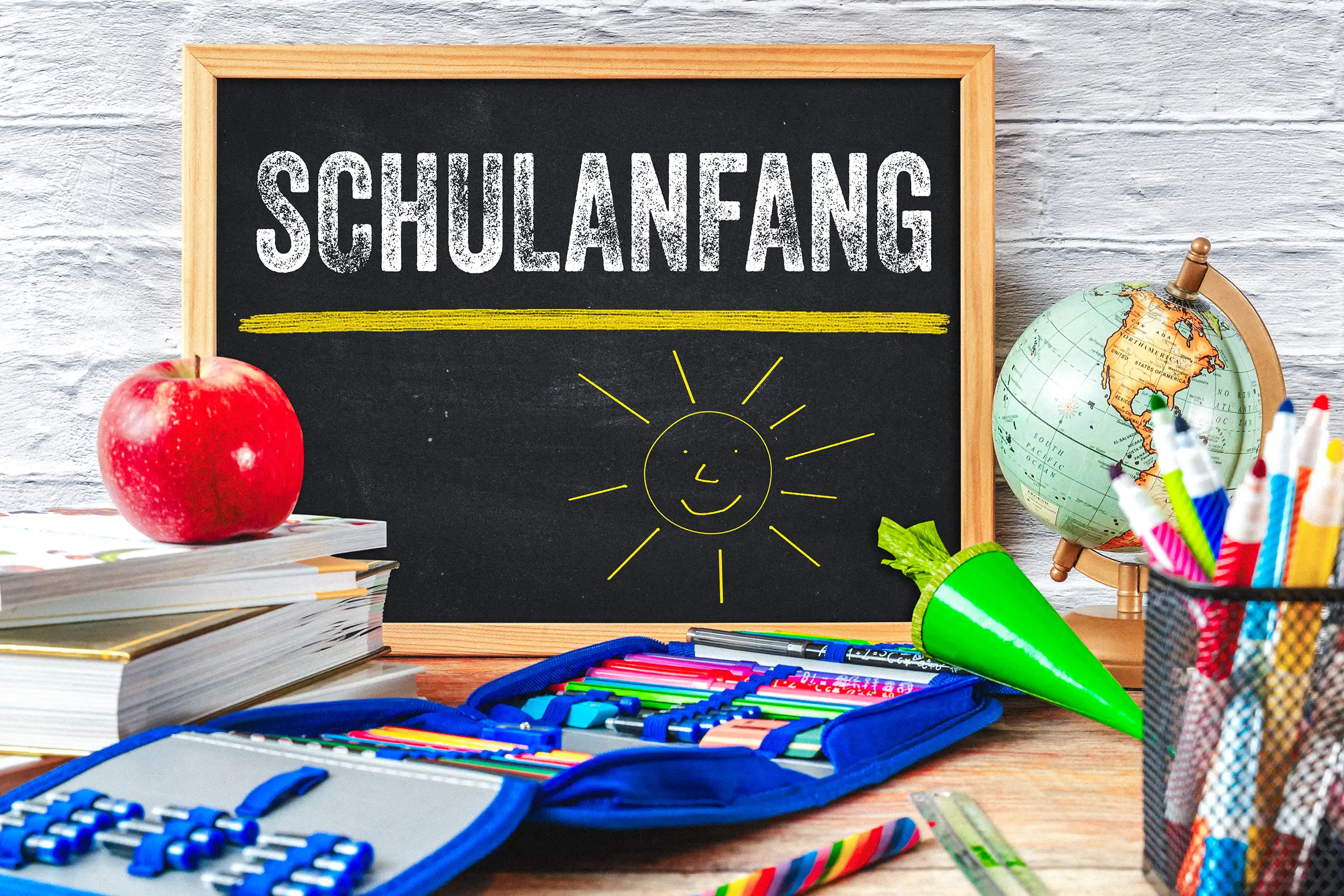 Schulanfang Bild mit Kreidetafel, lächelnder Sonne, Schultüte, Büchern, Globus und bunten Stiften als Gruß