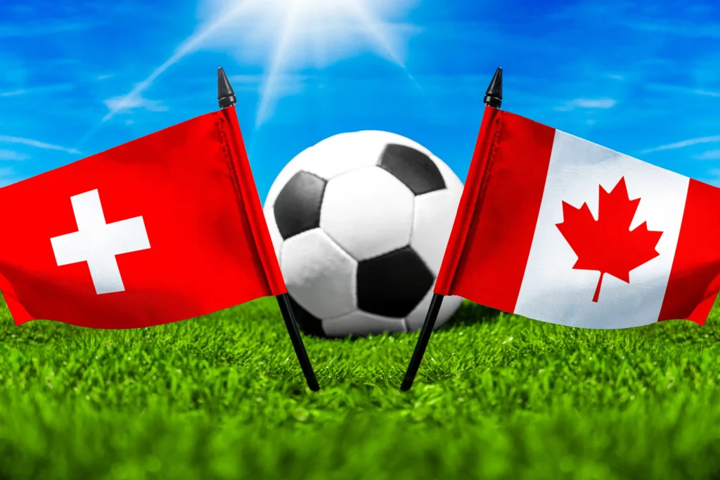 Schweiz- und Kanada-Flagge mit Fußball auf einem Rasenplatz vor blauem Himmel.