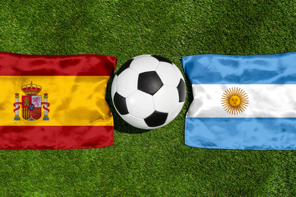 Spanien Argentinien mit Fußball zwischen den Nationalflaggen beider Länder auf grünem Rasen aus der Vogelperspektive.