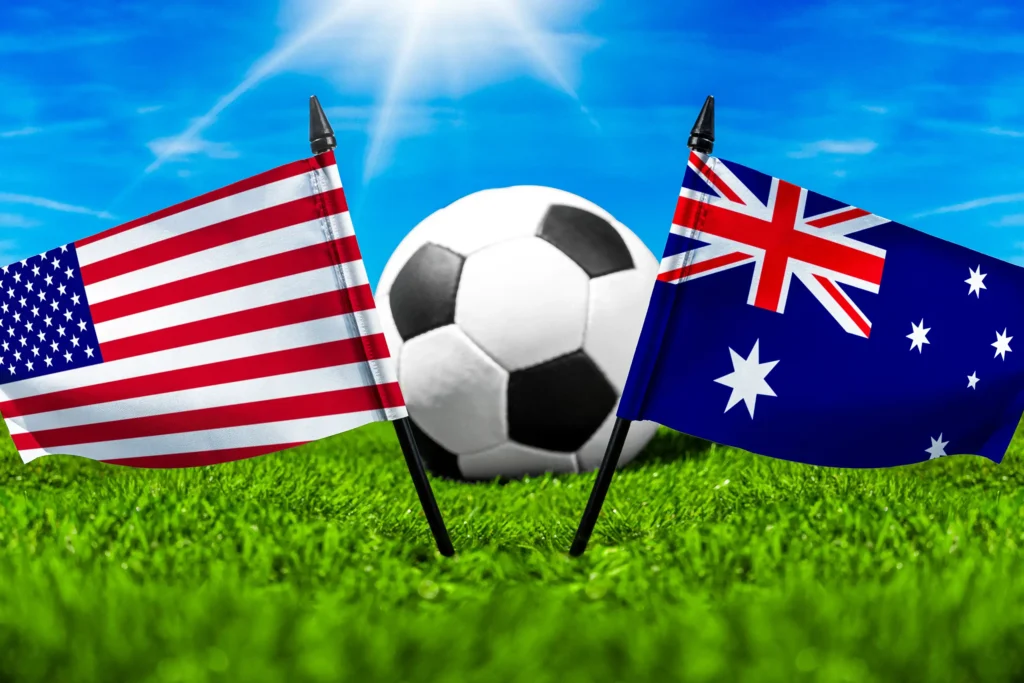 US-amerikanische und australische Nationalflagge neben einem Fußball auf einem Spielfeld mit grünem Rasen.